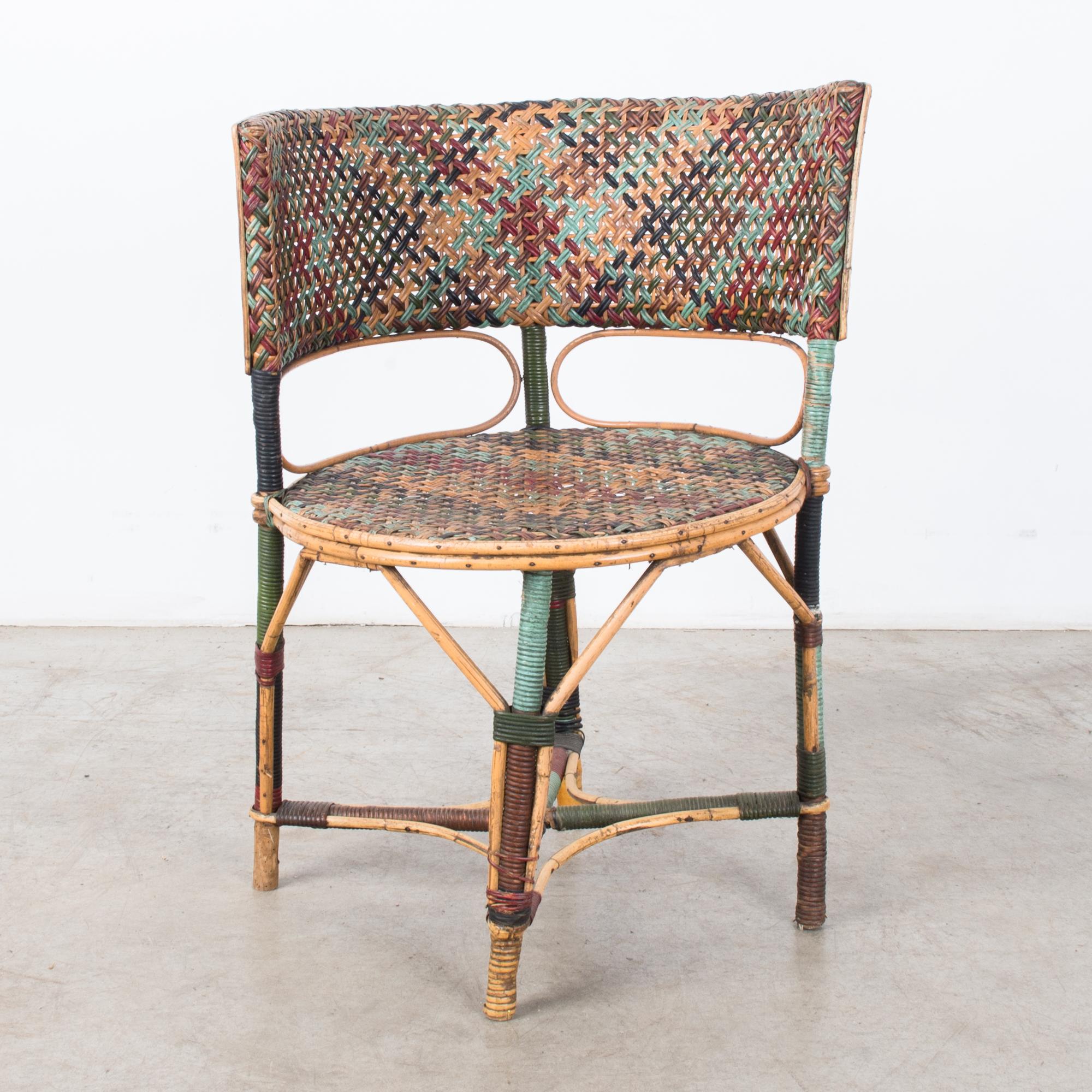 A 1920s French chair, made of colored rattan. A round seat and a curved backrest, with chair legs set in a diamond formation, creates a cubist bistro sensibility. A woven color palette of dark green, red and rust brown, black and teal blue, mixes