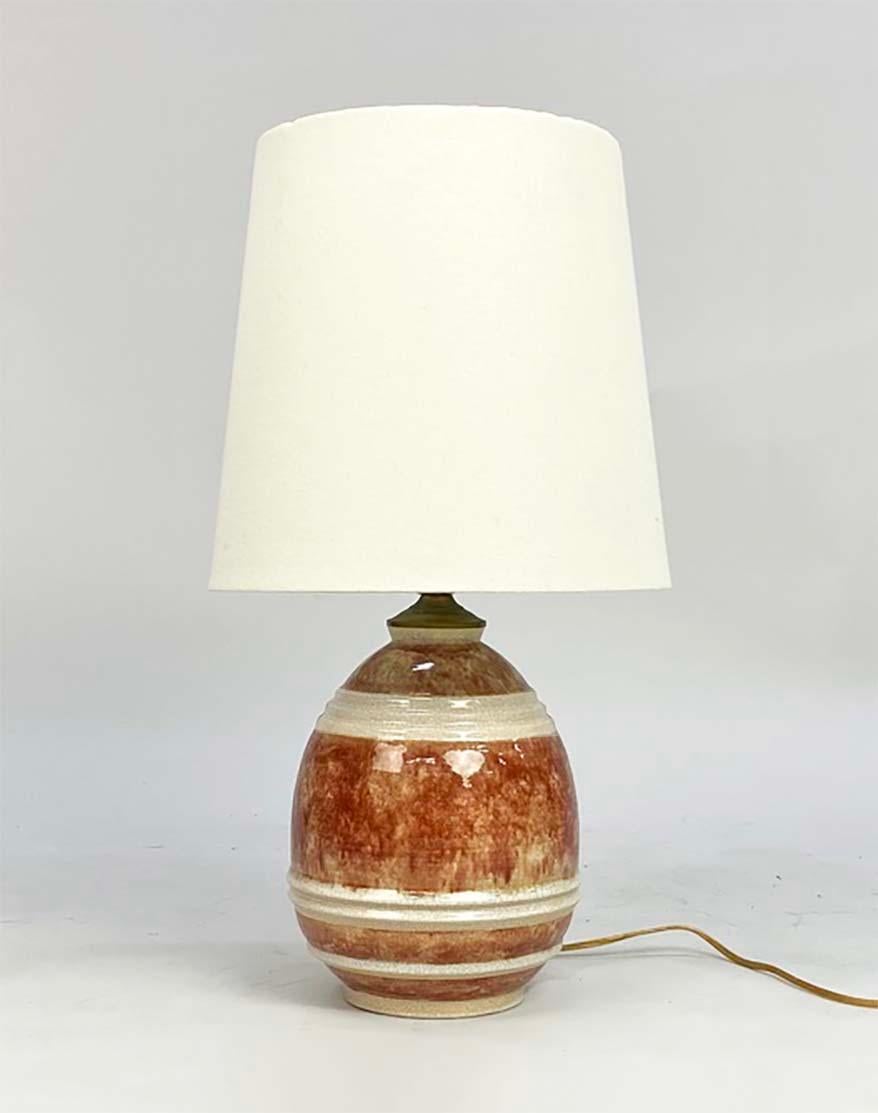 Voici une lampe simple, mais élégante, conçue par le céramiste français Marcel Guillard (1896-1932) et exécutée par Eleg Paris. Datant des années 1920, cet exemplaire présente une belle glaçure craquelée marron-rouge avec des bandes crème