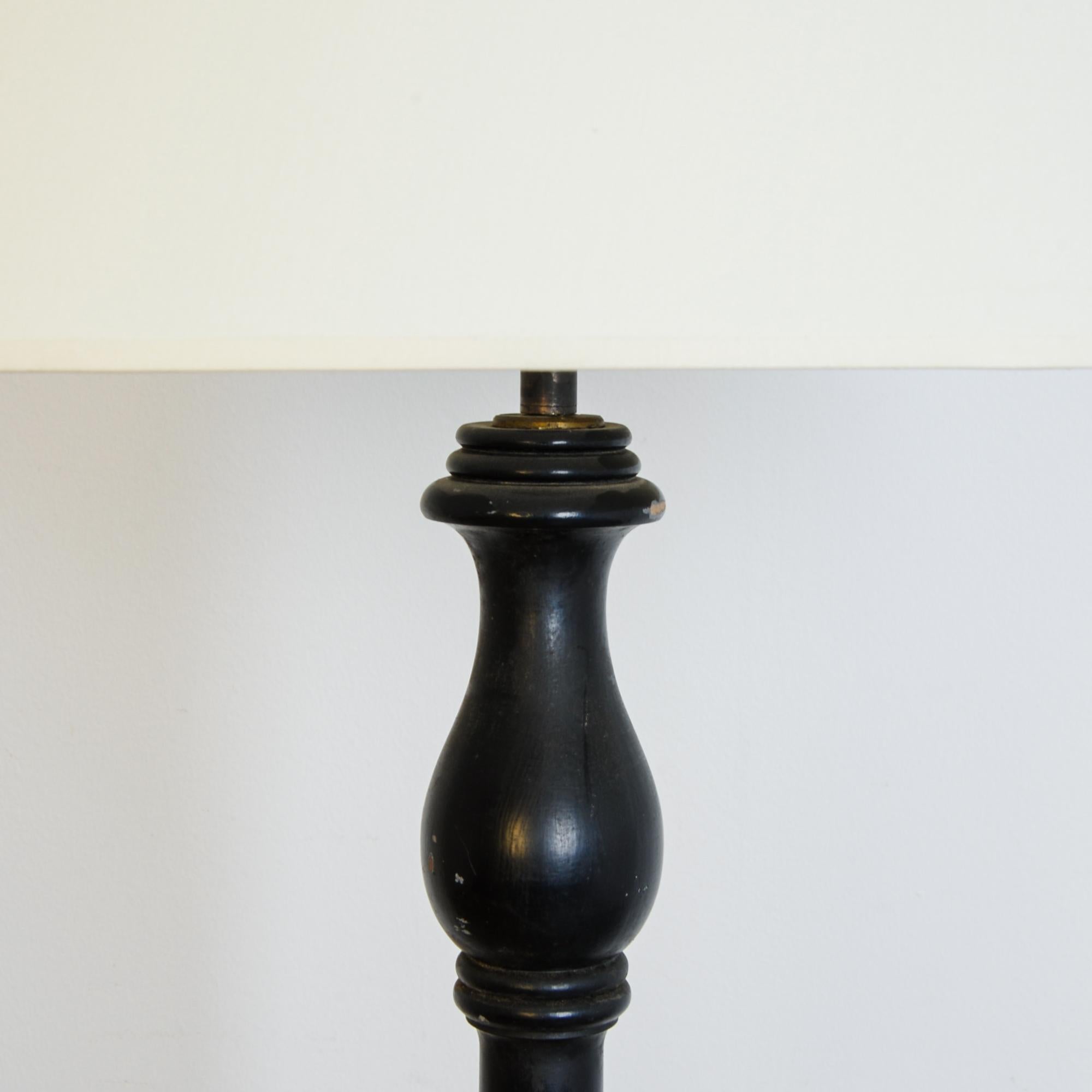 A black lacquer floor lamp from France, circa 1920. Influenced by a period revival fashion, this lamp shows a neoclassical architectural character, with turned ornamental segments, column and capitol, simplified and complimented by an aged patina.