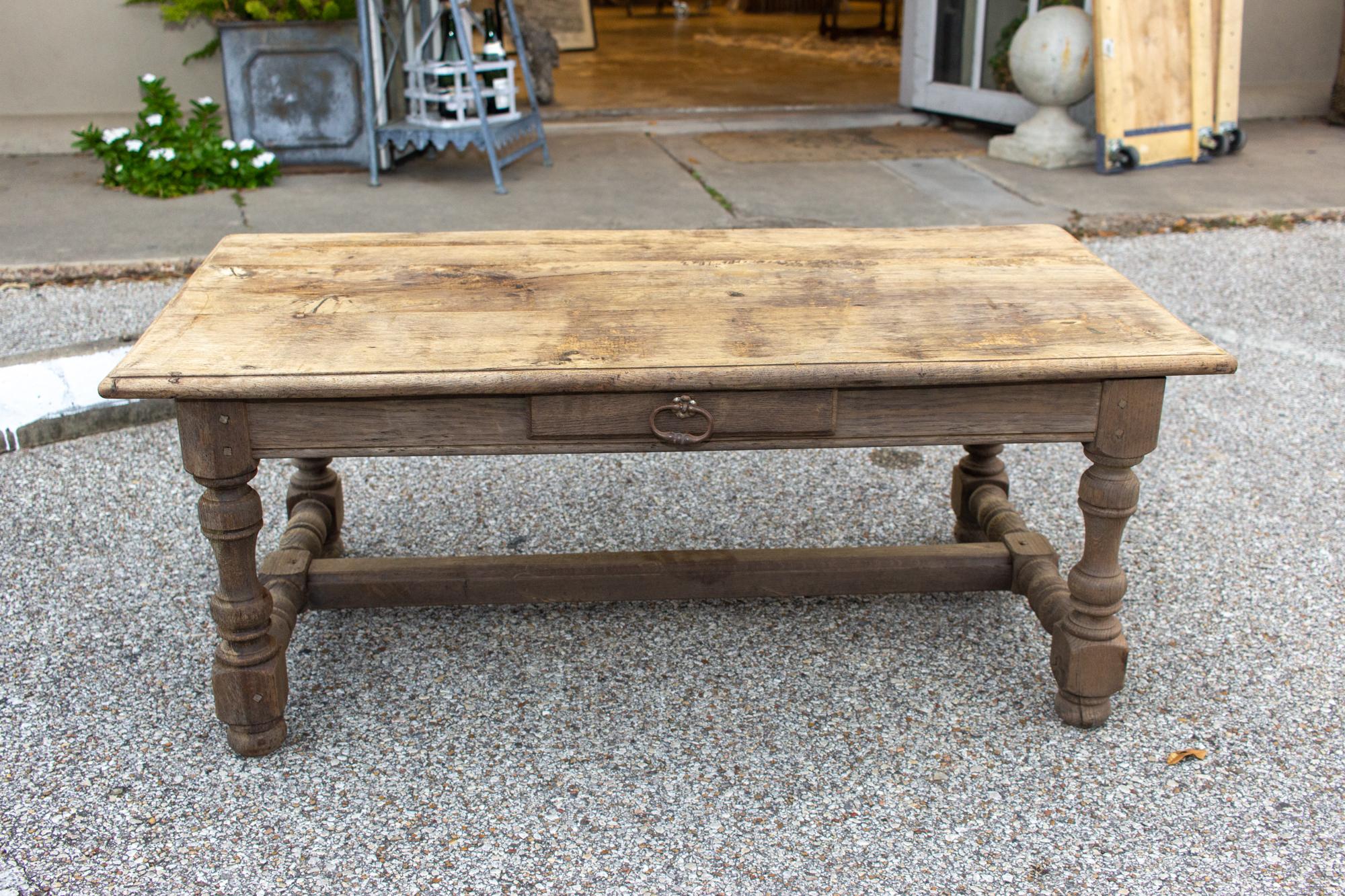 This distressed, solid oak coffee table was sourced in France and dates to the 1920s. The gray weathered finish to the wood is both beautiful and interesting. This coffee table has a single central drawer with a heavy iron ring-pull. There are