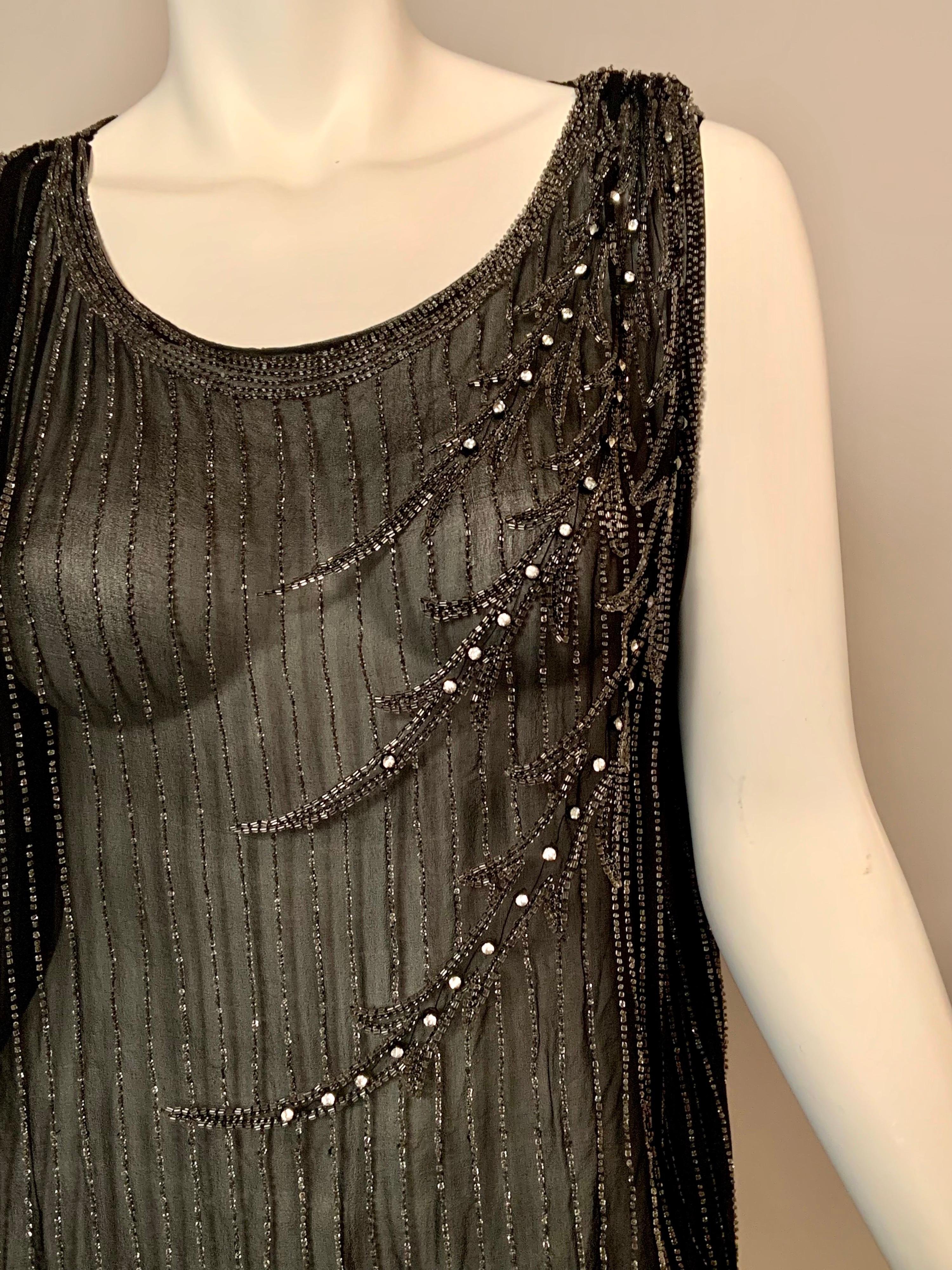 This beautiful French dress from the 1920's is black silk covered with a cascading vertical pattern of small bugle beads, looping back up at the hemline. This is a perfect backdrop for the curving beaded designs on the left side of the dress. These