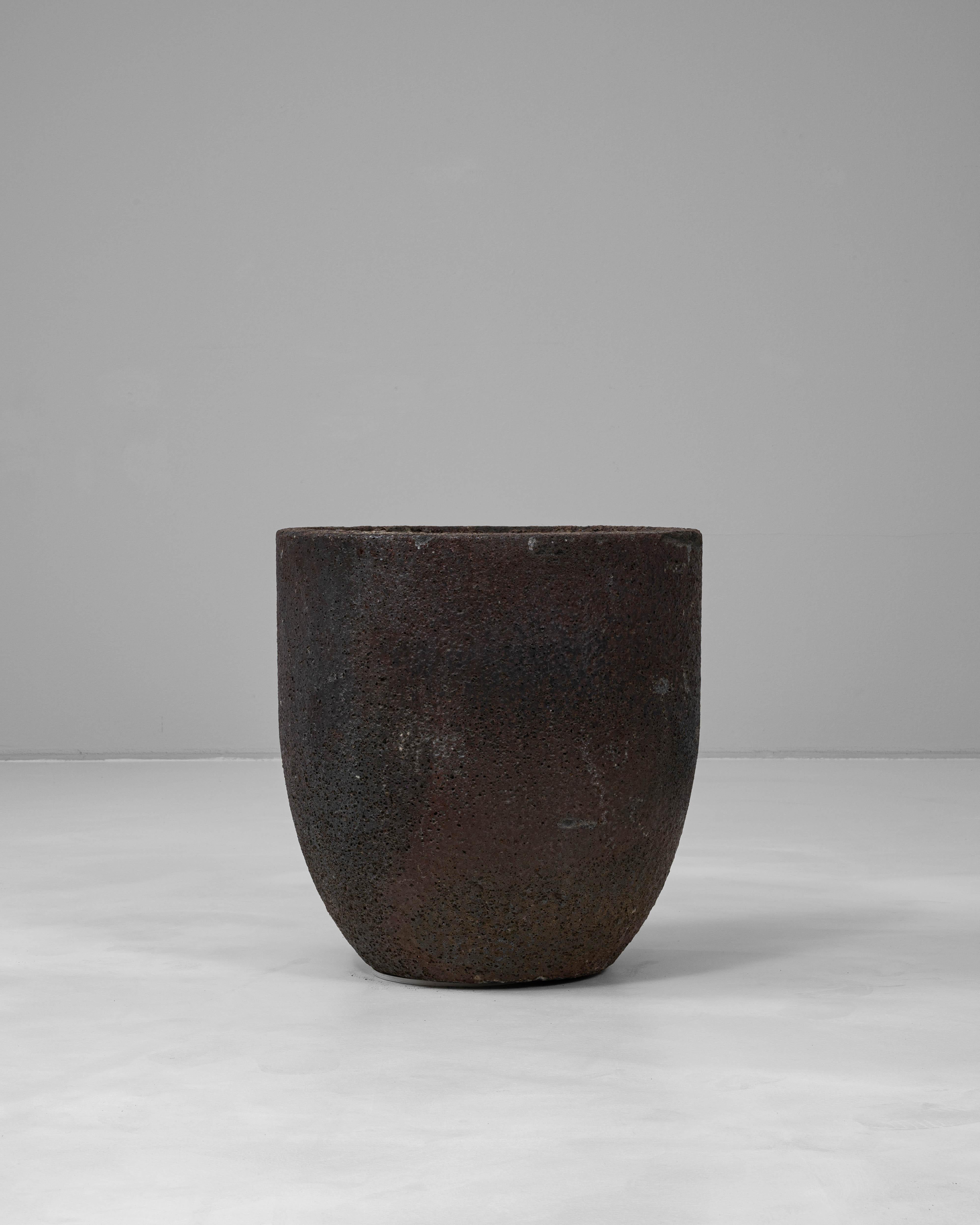 This 1920s French foundry crucible is a striking industrial artifact repurposed as sculptural decor. Originally used in metal casting, the piece is crafted from heavy, heat-resistant ceramic with a deeply textured, fire-patinated surface that ranges