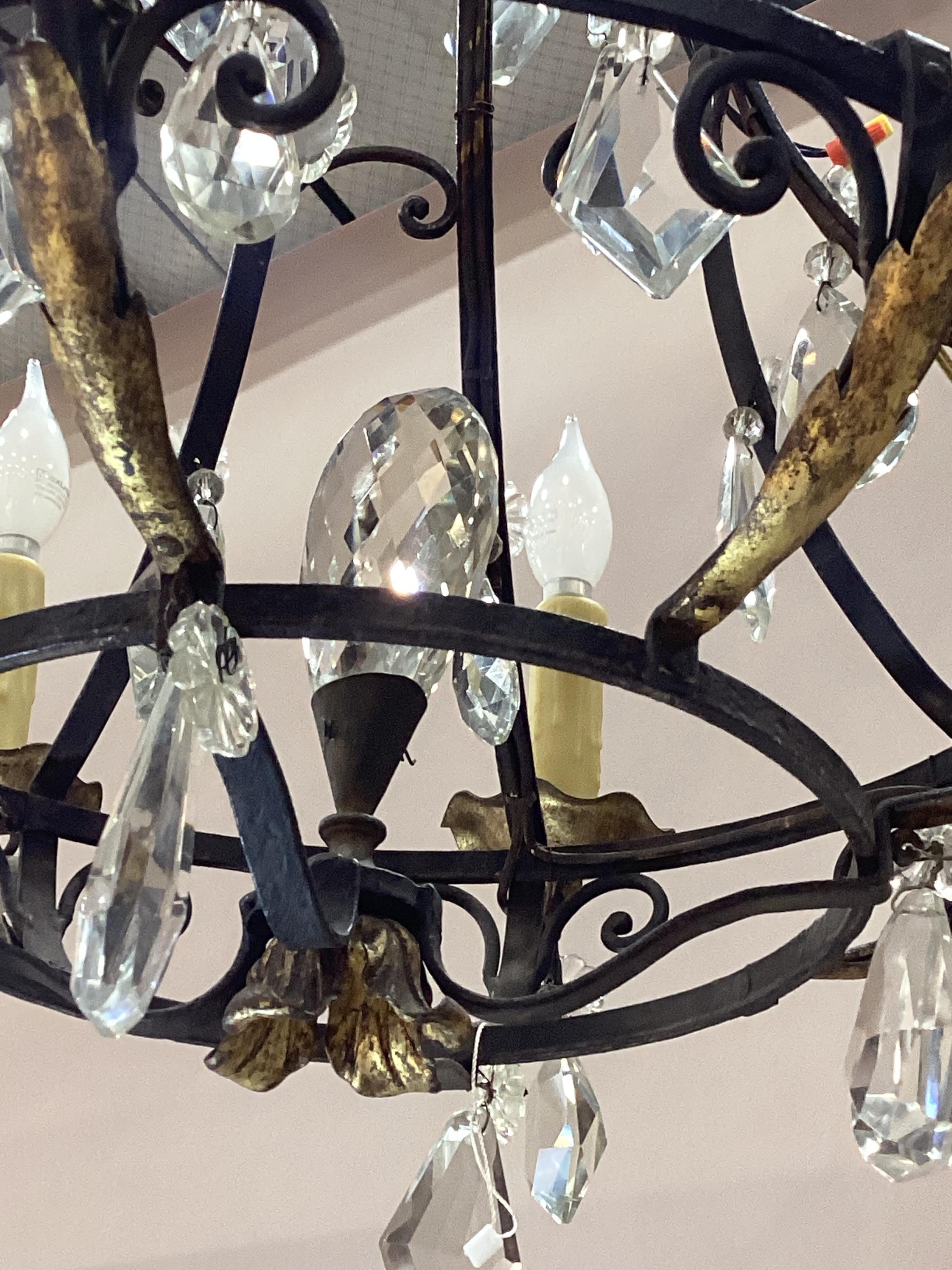 1920’s French Patinated and Gilt Iron Chandelier. Chandelier is adorned with faceted crystal drops. Wired and in good working condition.