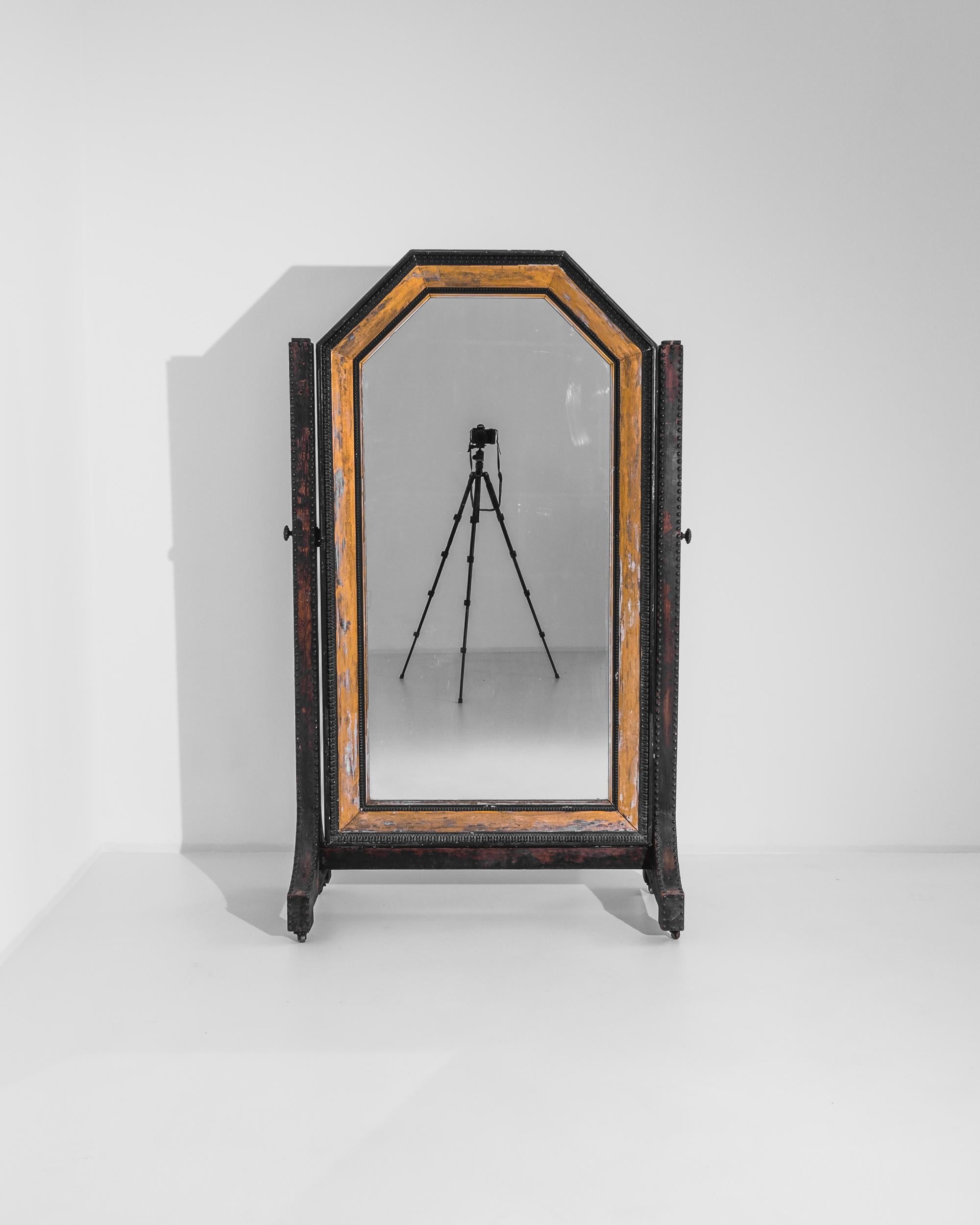 A large 1920s French wooden mirror on wheels. Flanked by two mulberry colored legs, this full length floor mirror offers a graceful reflection. Its combination of natural wood hue, black leaf pattern, and dark umber form a lively, yet contemplative