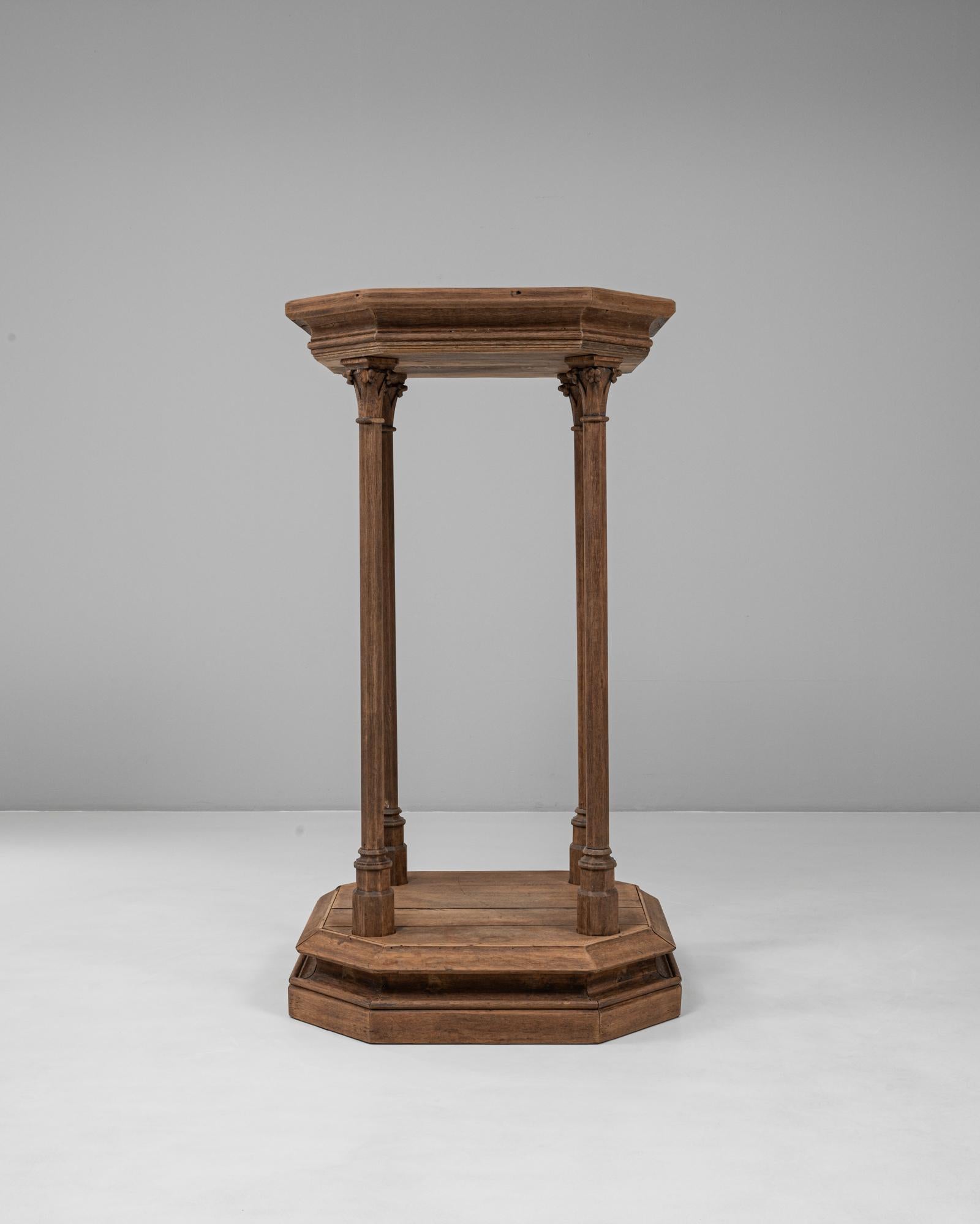 Questo piedistallo in legno del 1920 in stile gotico francese mostra un'influenza architettonica e una maestria impressionante. Realizzato in legno dai toni intensi, il pezzo presenta una base ottagonale che sostiene sei sottili colonne con