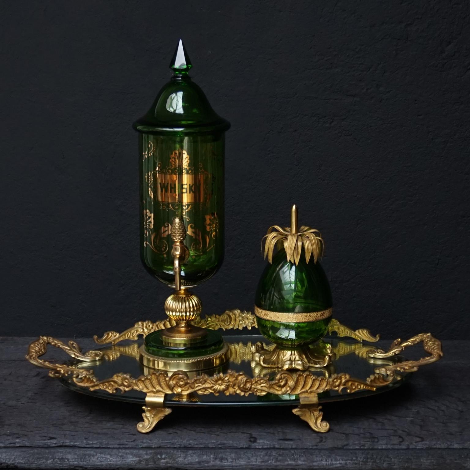 Antiguo juego de bar Hollywood Regency francés de cristal verde y bronce dorado sobre bandeja de espejo.
En la bandeja, un cuenco con tapa de piña y un dispensador de whisky con grifo. 

Juego pesado muy bonito con un cuenco de cristal verde con