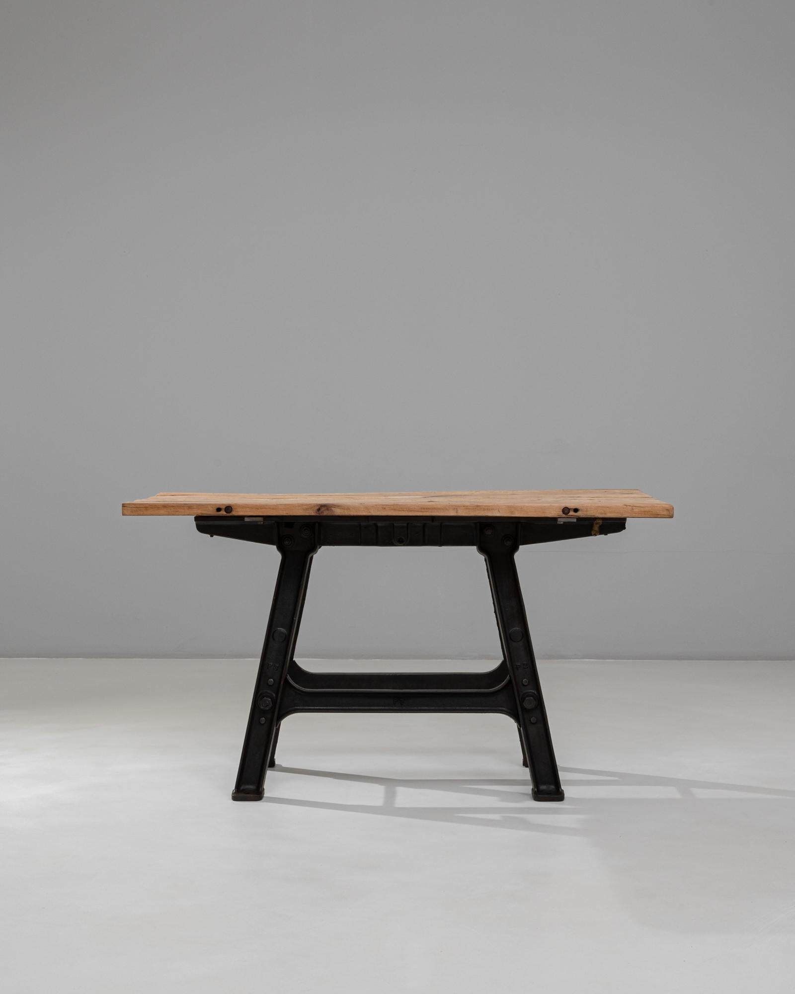 Esta mesa industrial francesa de hierro de los años 20 con tablero de madera muestra una sorprendente mezcla de ingeniería utilitaria y calidez natural. La robusta base de hierro negro presenta patas angulares, juntas remachadas y refuerzos