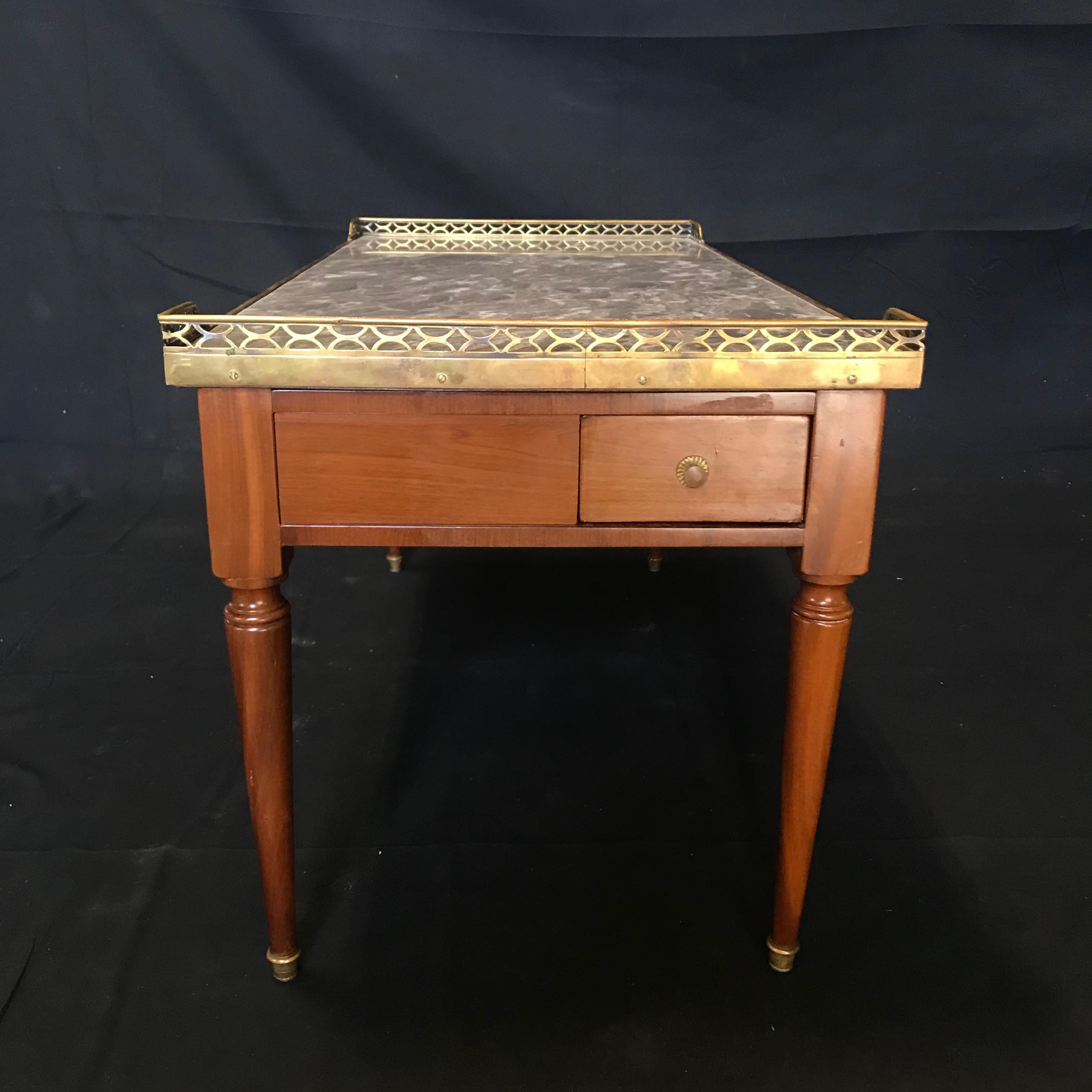 Elegant classic French Louis XVI style coffee table having gold fretwork around a gorgeous gray Italian marble top with walnut base and tapered legs. The single drawer at one end is a surprising beautiful touch.
#5823
H skirt 13”.
 