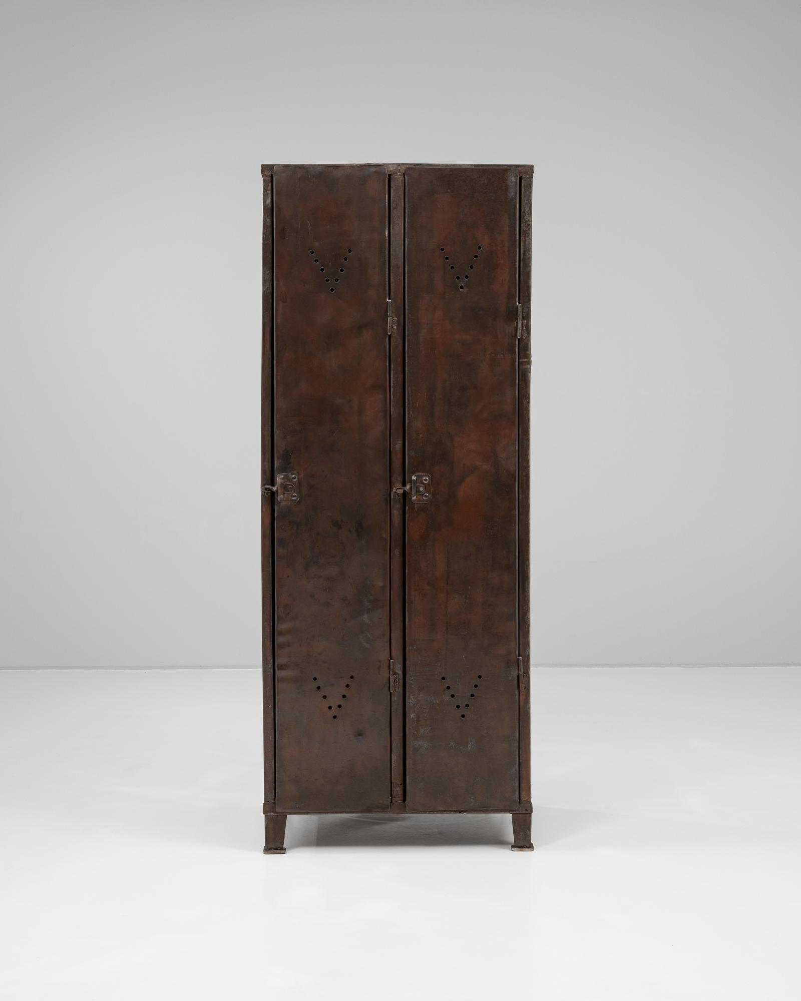 This 1920s French metal cabinet exemplifies early 20th-century industrial design with a raw, utilitarian aesthetic. Crafted from solid sheet metal with a naturally aged, oxidized finish, the cabinet features double doors with diamond-patterned