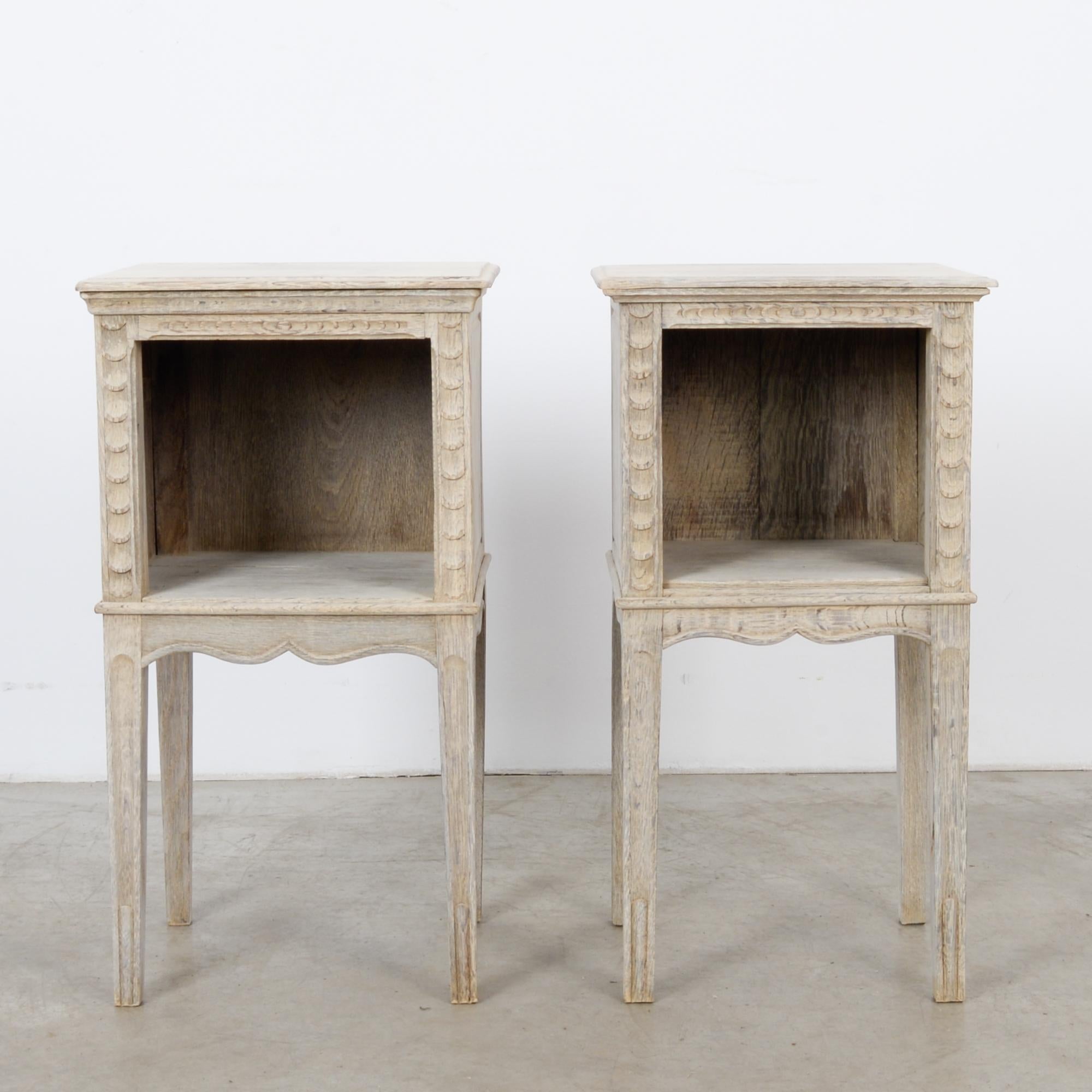 This pair of bleached oak side tables was made in France, circa 1920. They stand on slightly tapered and angular legs featuring ridges at the bottom. The scalloped apron and moldings on all sides show off its outstanding craftsmanship. With a shelf