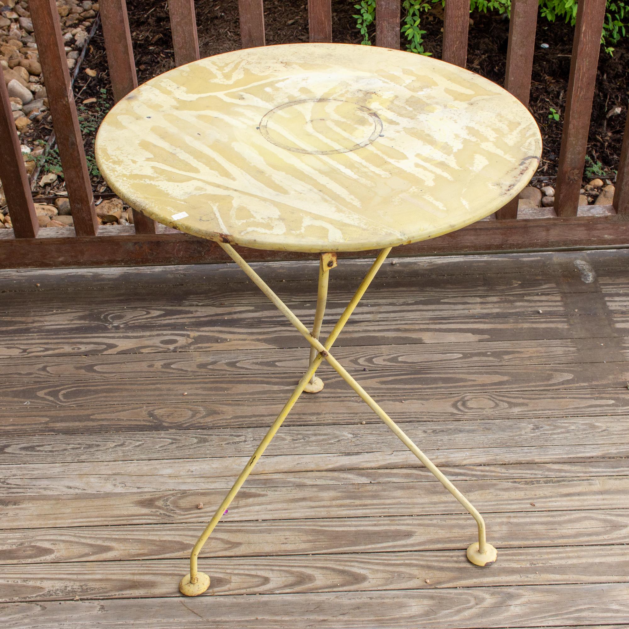 This 1920s French metal bistro table is painted pale yellow and has a tripod-style base. The top is weathered and patinated with time and age and was likely used outdoors. This lightweight table is easily moved around wherever needed, and could make