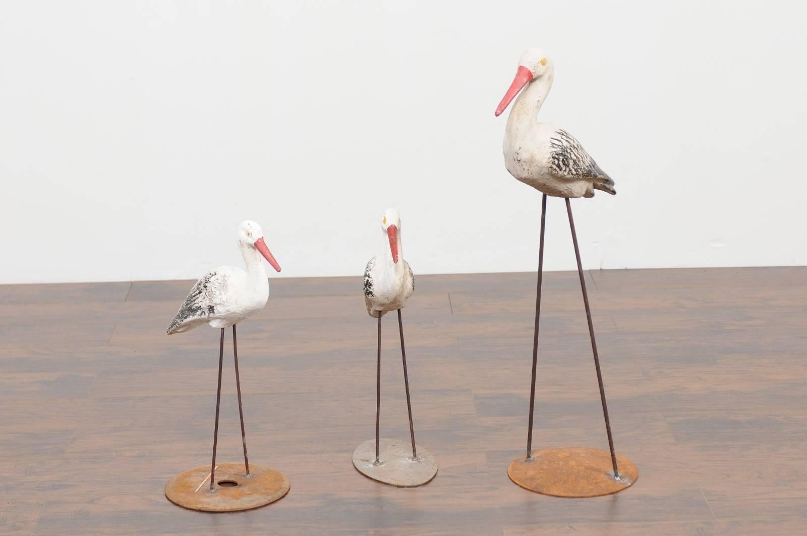 A grouping of three French painted stone storks from Alsace from the early 20th century, mounted on iron bases and sold individually. Discover the charm of Alsace with this captivating grouping of three French painted stone storks, each a symbol of