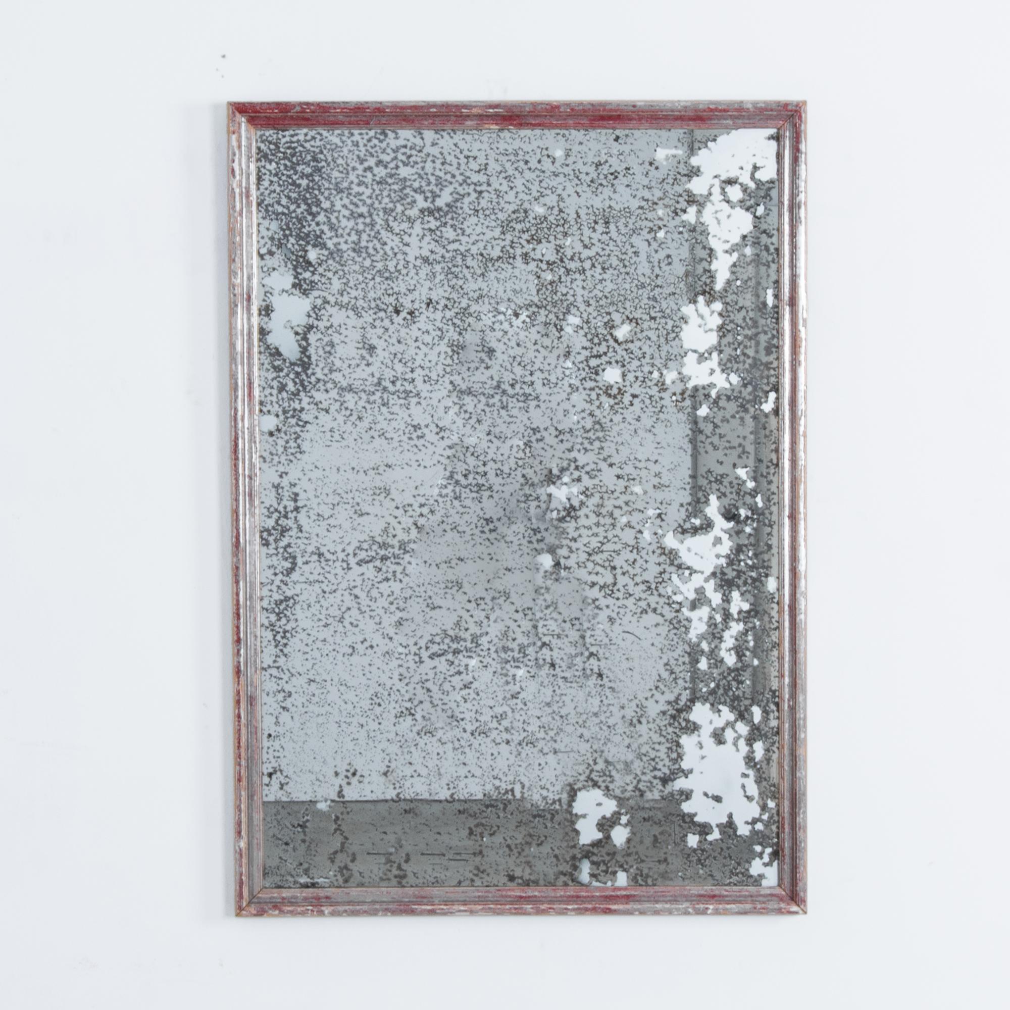This wall mirror from France, circa 1920, has a heavy, variegated patina. Dark speckles cover the entirety of the surface of the mirror, creating a nostalgic, mysterious effect. The worn red paint of the rectangular wooden frame implies a vivid past.