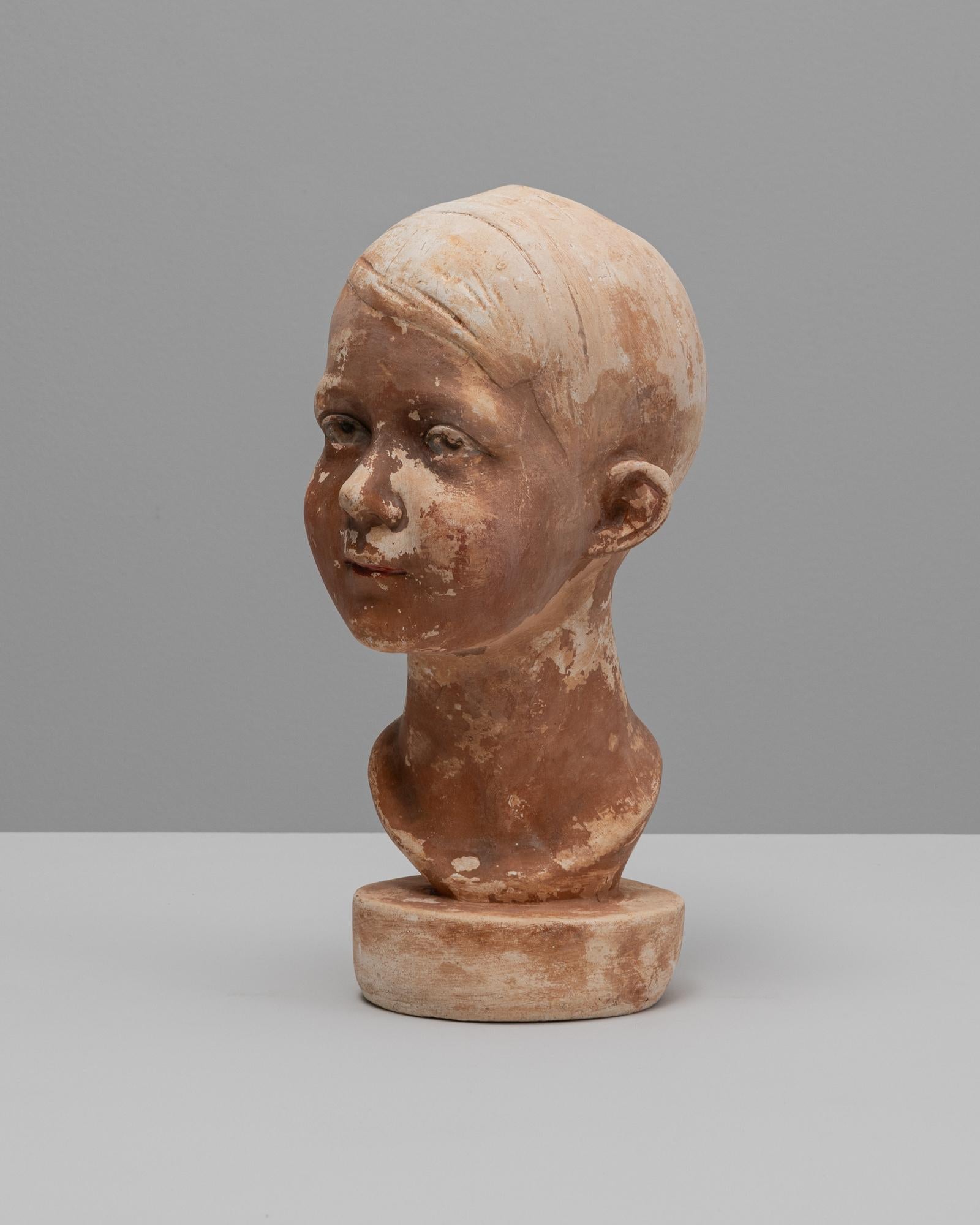 Questo busto in gesso francese di un ragazzo degli anni '20 cattura la tranquilla sensibilità e il naturalismo caratteristici della scultura decorativa del primo Novecento. La figura è resa con tratti delicati del viso e un'espressione morbidamente
