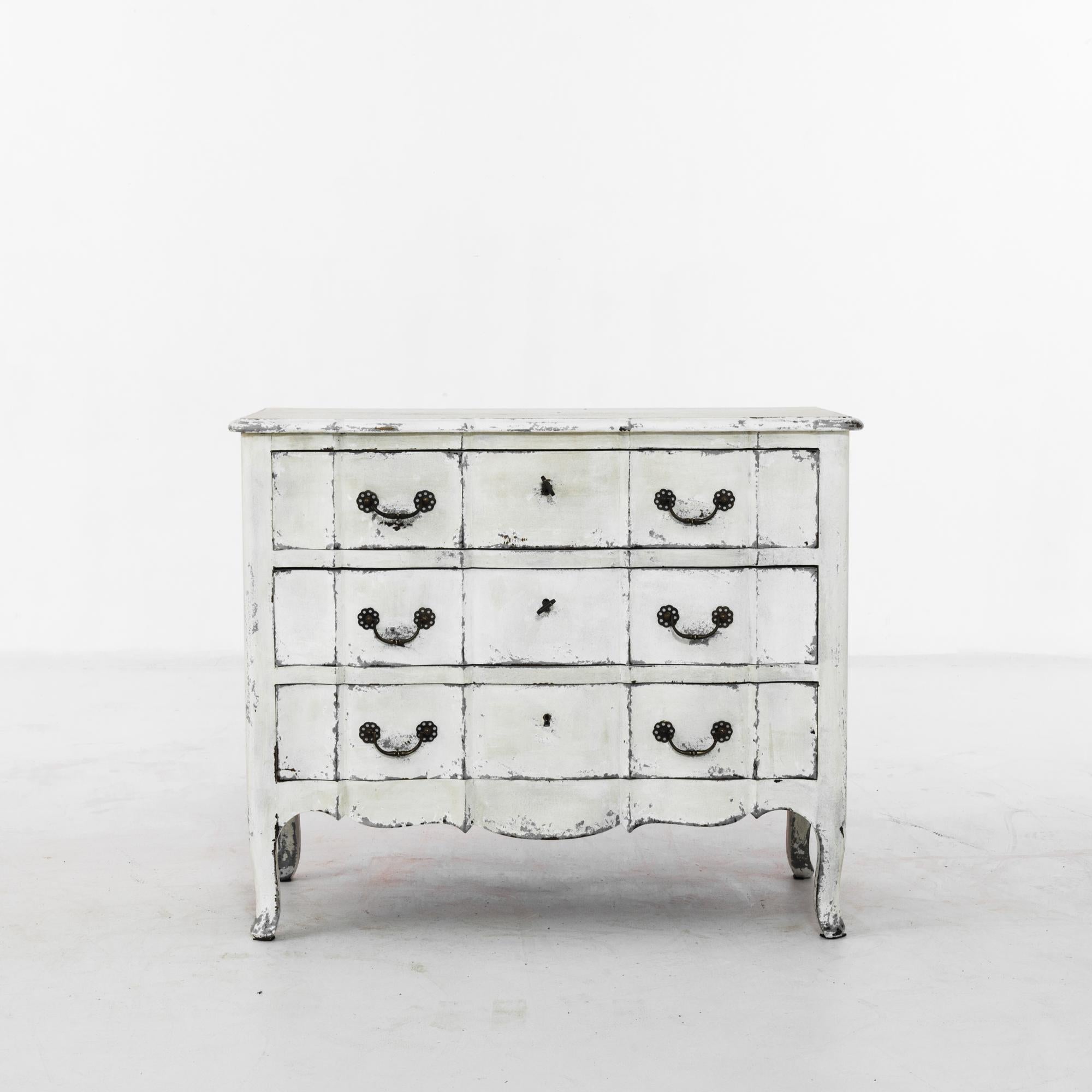 This wooden chest of drawers was made in France, circa 1920. Cabriole legs and a scalloped apron give it a French Provincial touch. The chest houses three drawers, with locks for the upper two. Finished with a distressed white patina, highlighting