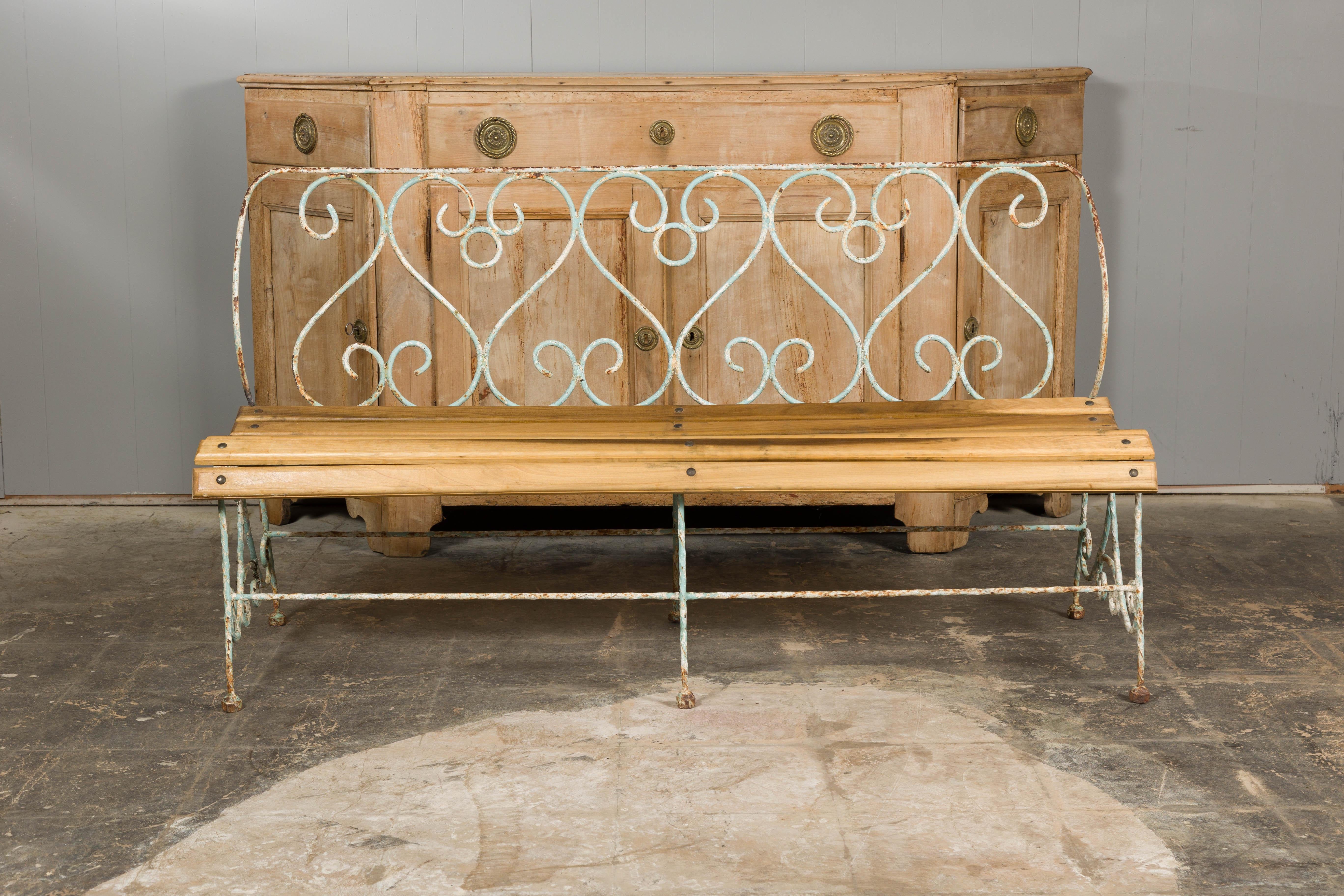 A French rustic, painted iron garden bench from the 19th century with scrolling motifs on the back, curving slatted seat and great weathered appearance. This 19th-century French rustic painted iron garden bench exudes a timeless charm, effortlessly