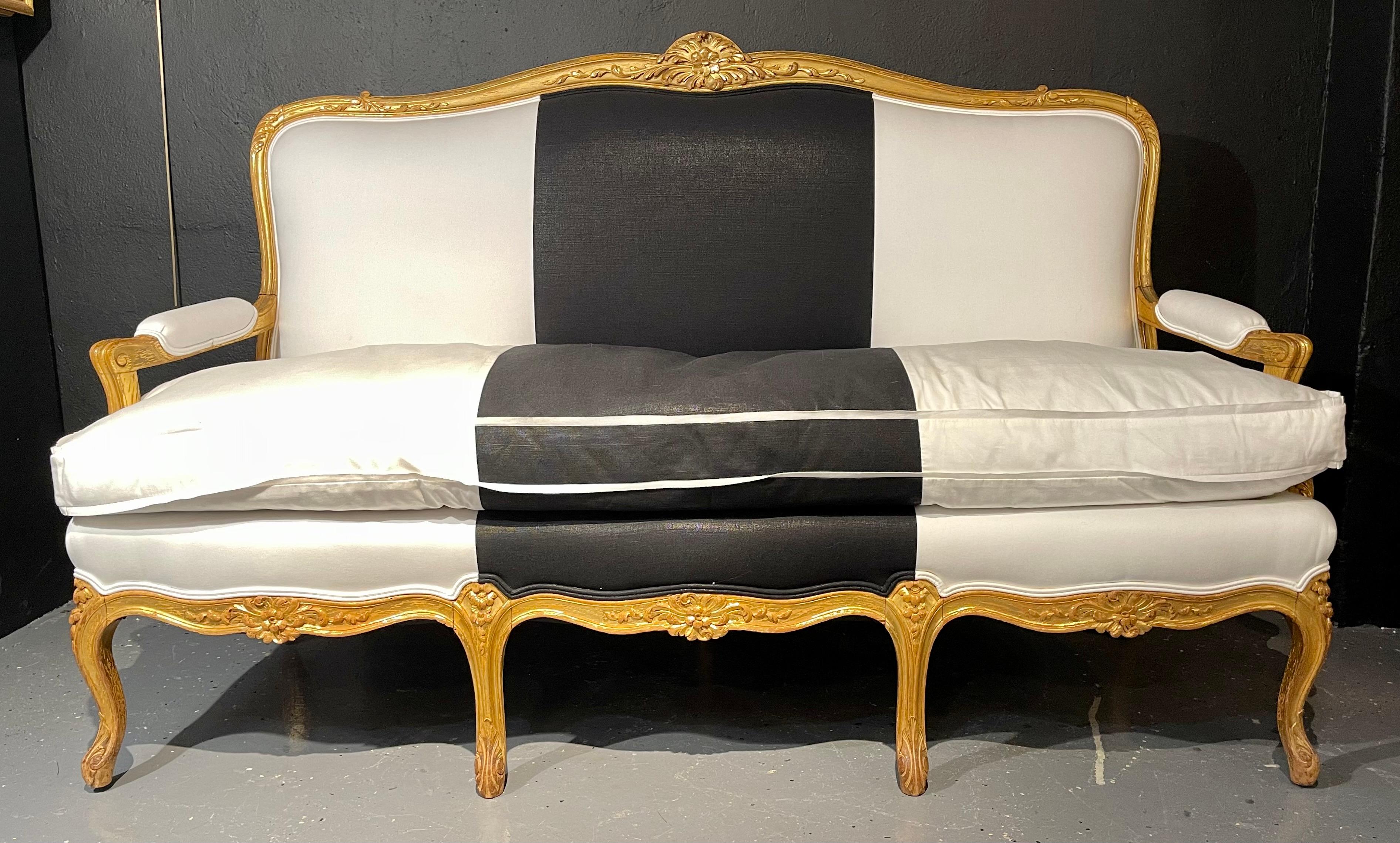 1920s French gilt wood upholstered settee, canape or sofa in black and white polished cotton. One of a compatible pair of finely carved and detailed water gilt decorated Louis XV style canapes or loveseat sofas.
A simply stunning compatible pair
