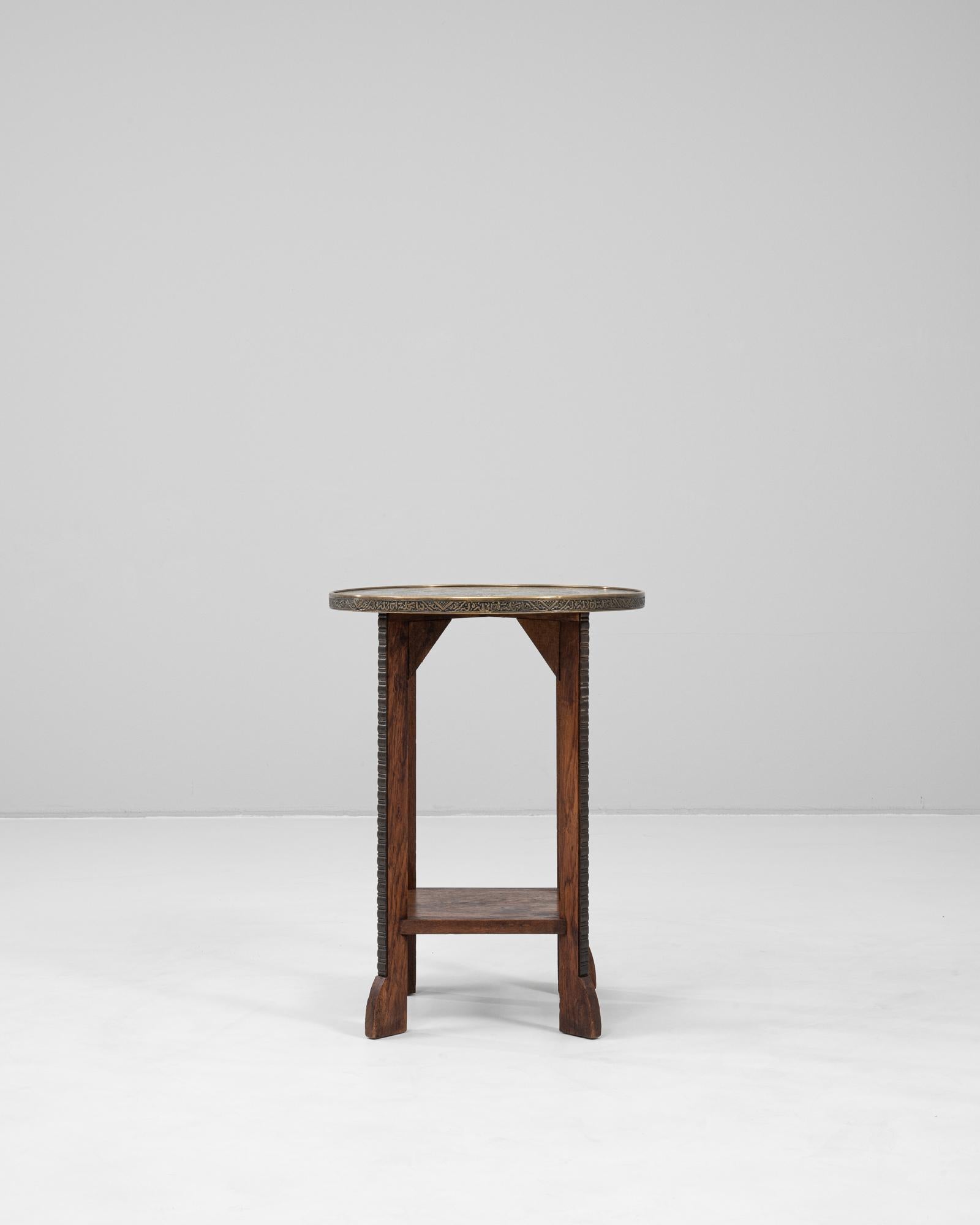 This 1920s French side table features a richly detailed repoussé brass top inset with intricate engravings of athletic and technological motifs, likely celebrating early 20th-century advancements and sporting events. The circular tabletop is