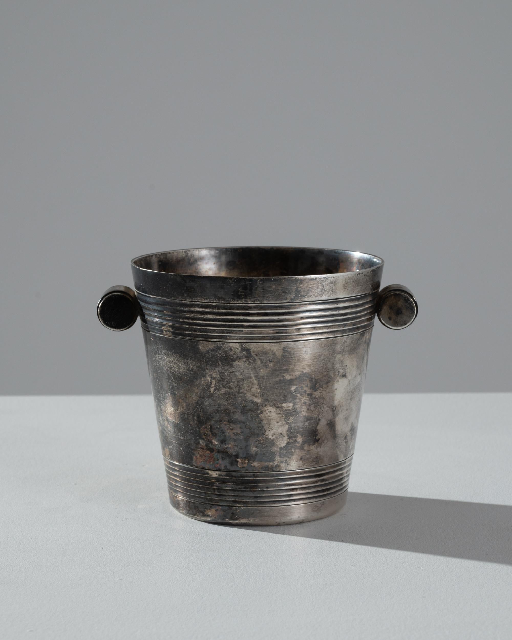 This vintage ice bucket evokes the glamorous parties of the roaring 20s. Made in France in the 20th century, its function harks back to a time when ice was still a precious commodity. This fact is reflected in the use of silver plate tarnished and