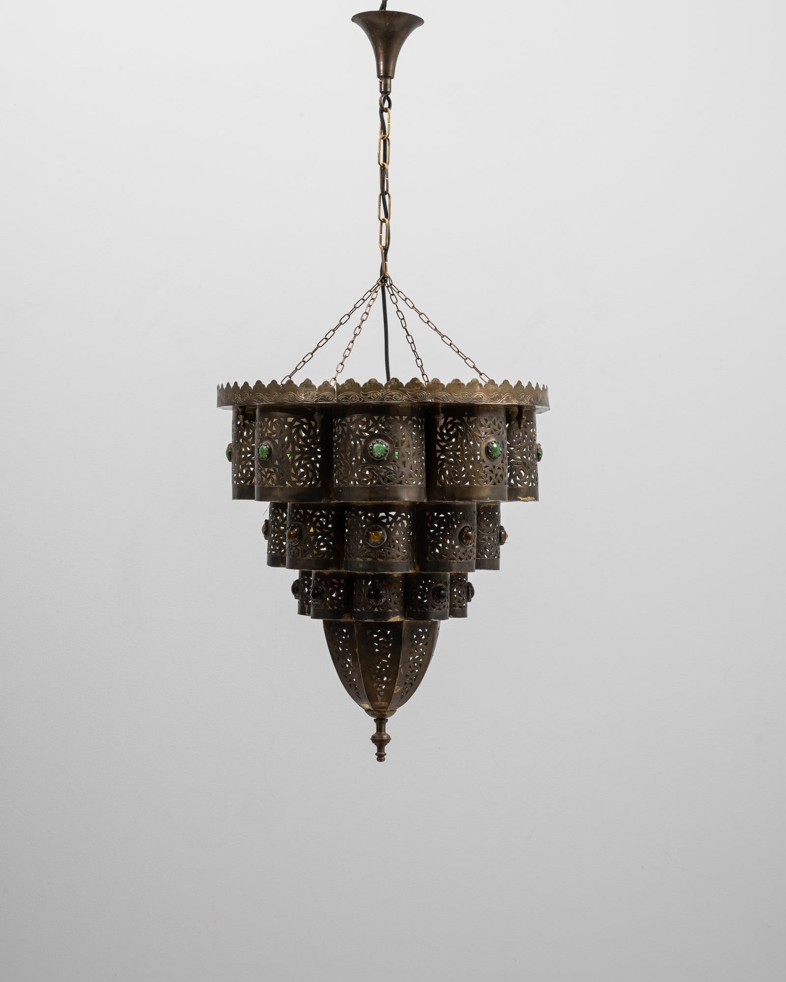 Questo lampadario a sospensione francese in ottone a più livelli degli anni '20 è un esempio straordinario di artigianato dei primi del Novecento, che fonde la lavorazione del metallo ornato con accenti di vetro decorativo. Il lampadario presenta un