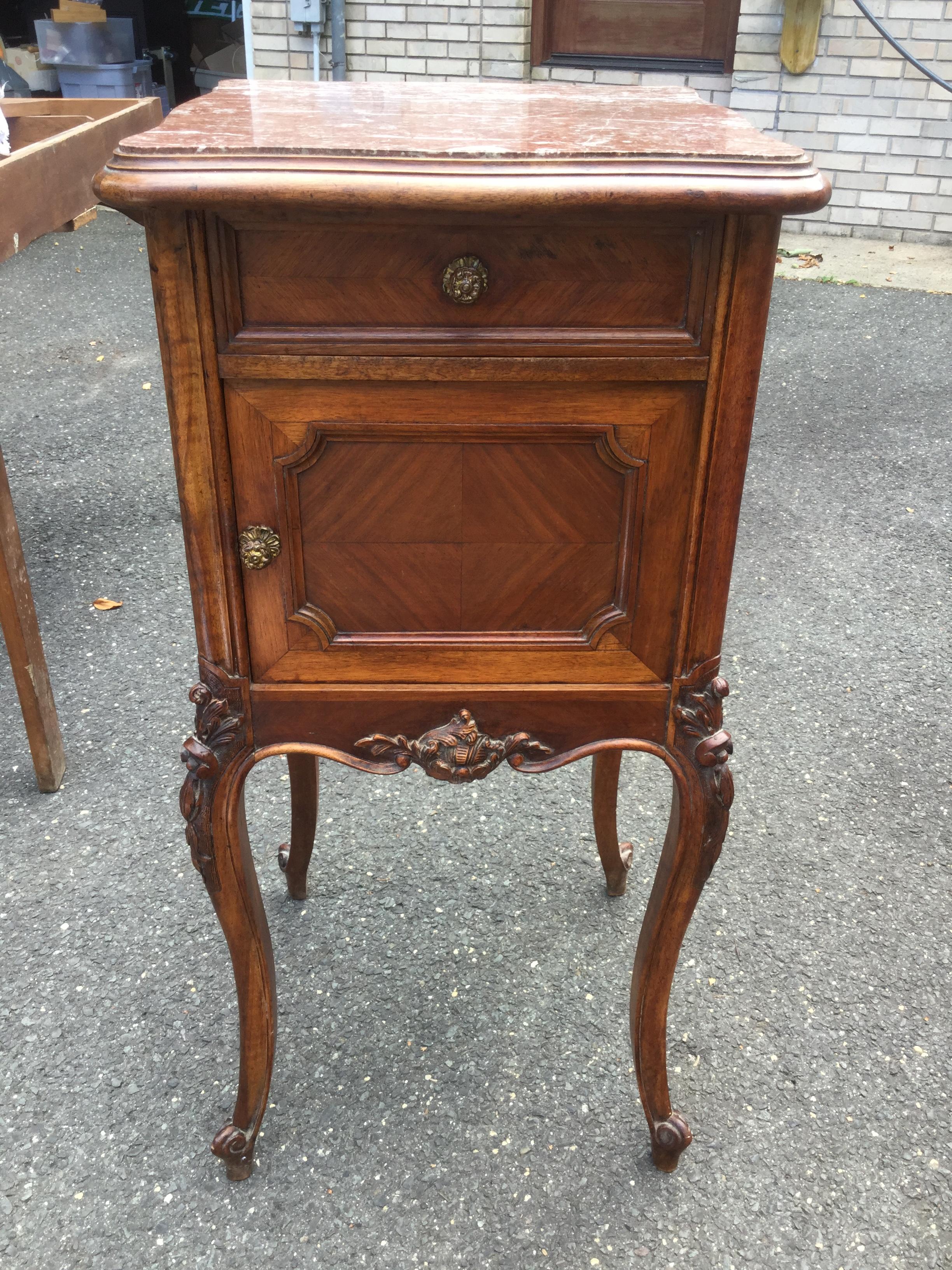 Charming French Louis XV-style night/side table. With a marble top, this is the perfect bed-side or sofa-side table. Floral motif carvings adorn the top and bottom legs. There is one drawer, and the door features marquetry while concealing a