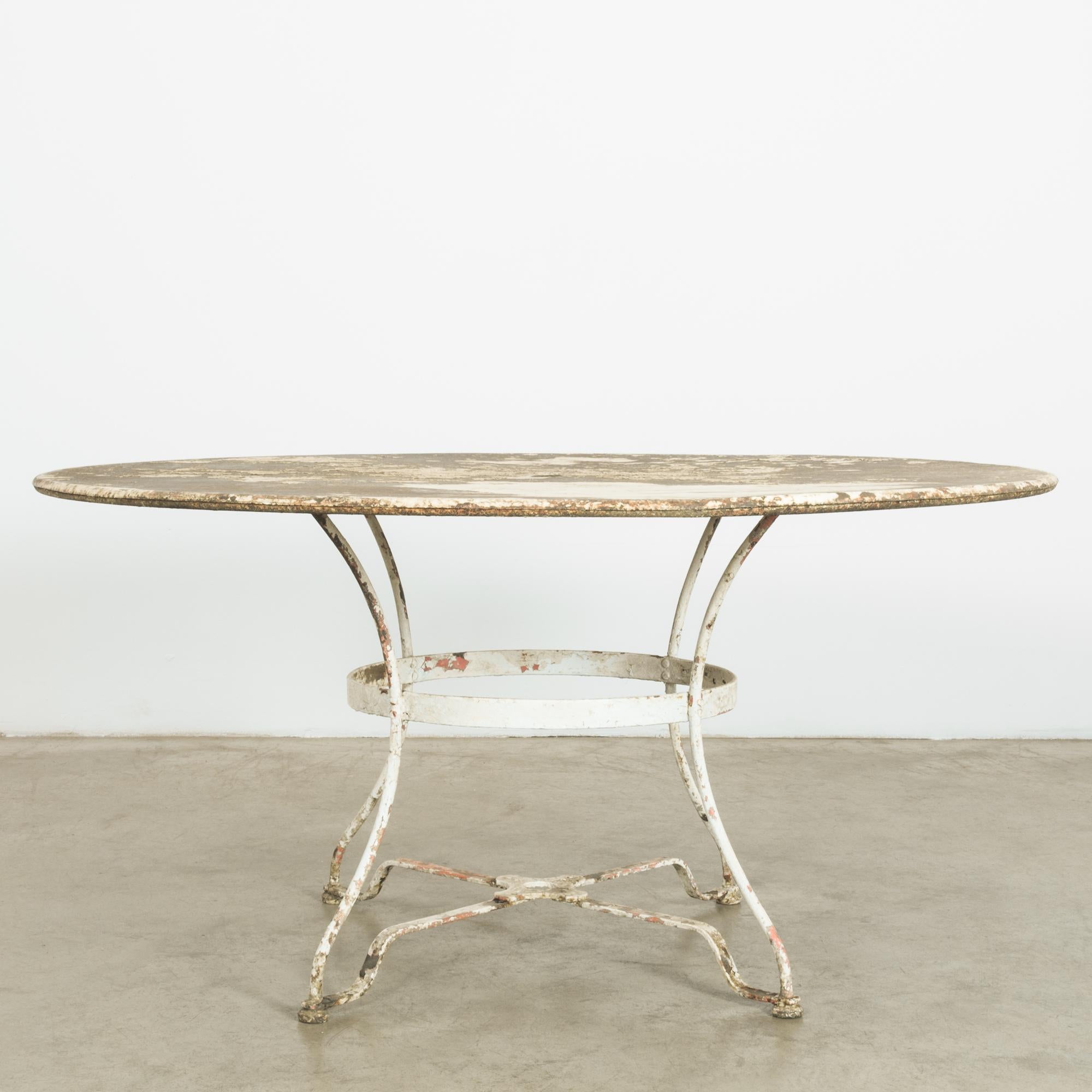 A white patinated metal table from France, produced circa 1920. Four parabolic legs, connected by umbrella stand fixture, support a broad tabletop with original patination. Sun-drenched and marvelously aged, this charming garden table sings of blue