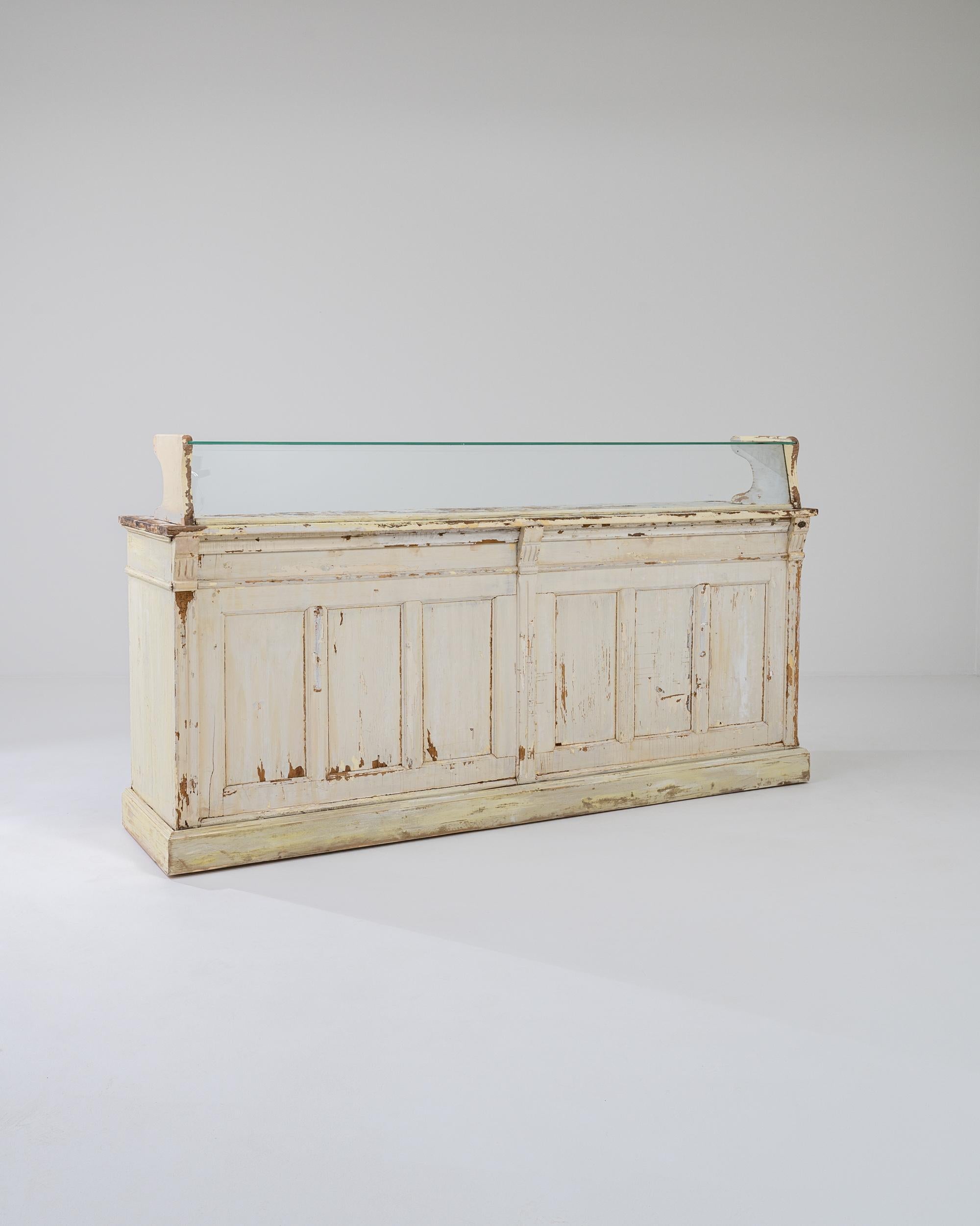 This vintage wooden bar offers an enchanting period piece. Made in France in the 1920s, it would likely have been used as a display case in a shop; a glass window protects the counter, shielding the delicate items on offer. A deep recess with a