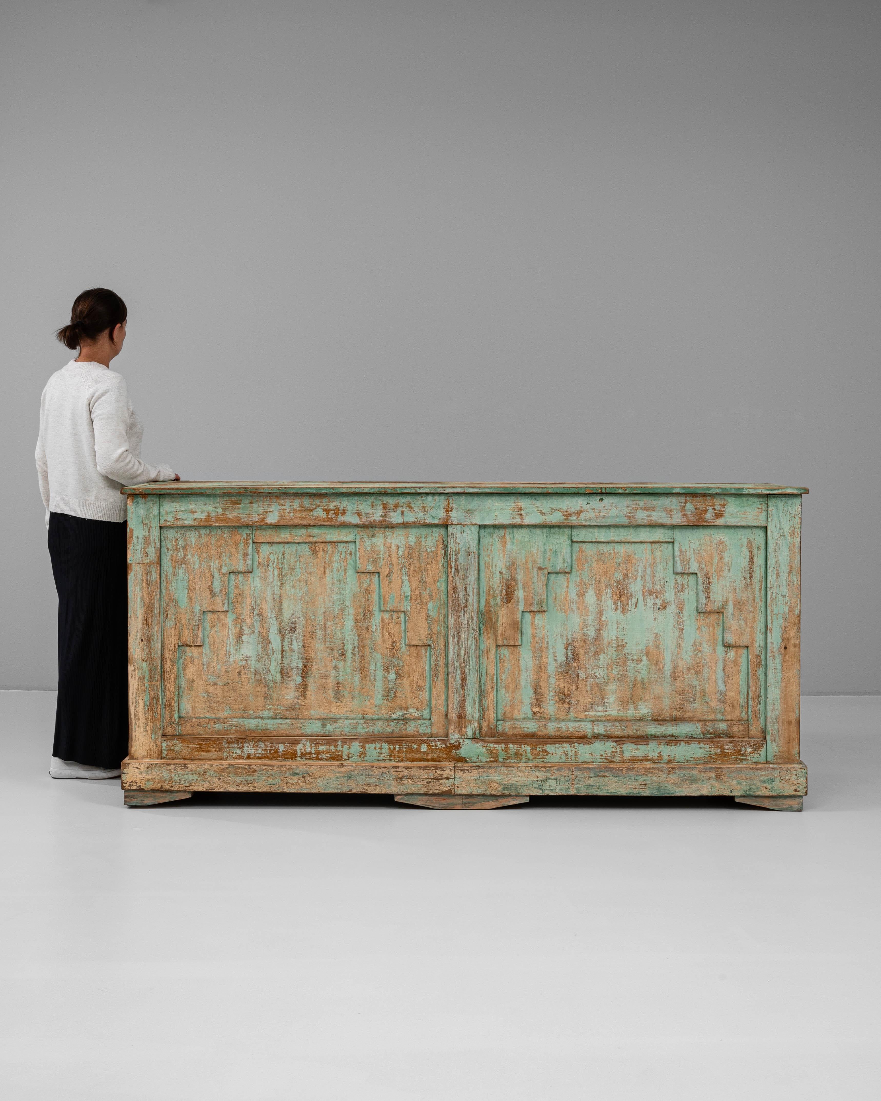 This 1920s French wooden bar is a vibrant expression of Art Deco influence, distinguished by its striking geometric paneling and original turquoise patina. The hand-carved façade features stepped linear motifs, lending architectural depth and a