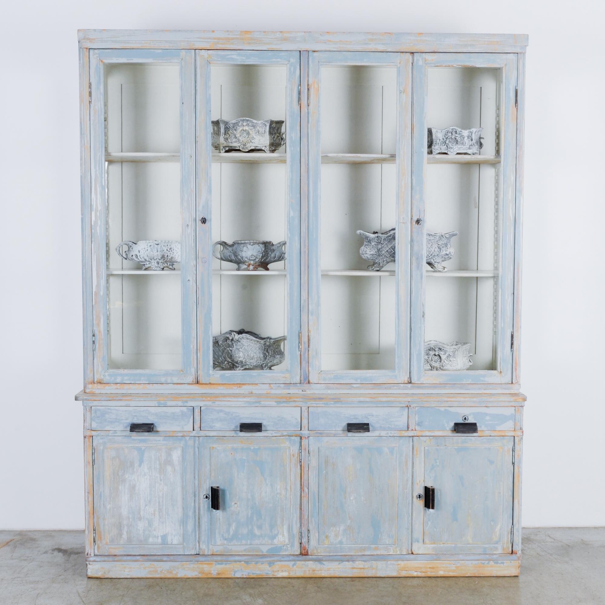A wood patinated vitrine produced in France, circa 1920. This elegantly aged cabinet features four glass panel doors, four drawers, and four cabinet doors below. At eight feet tall and over six feet wide, this towering vitrine commands the room with