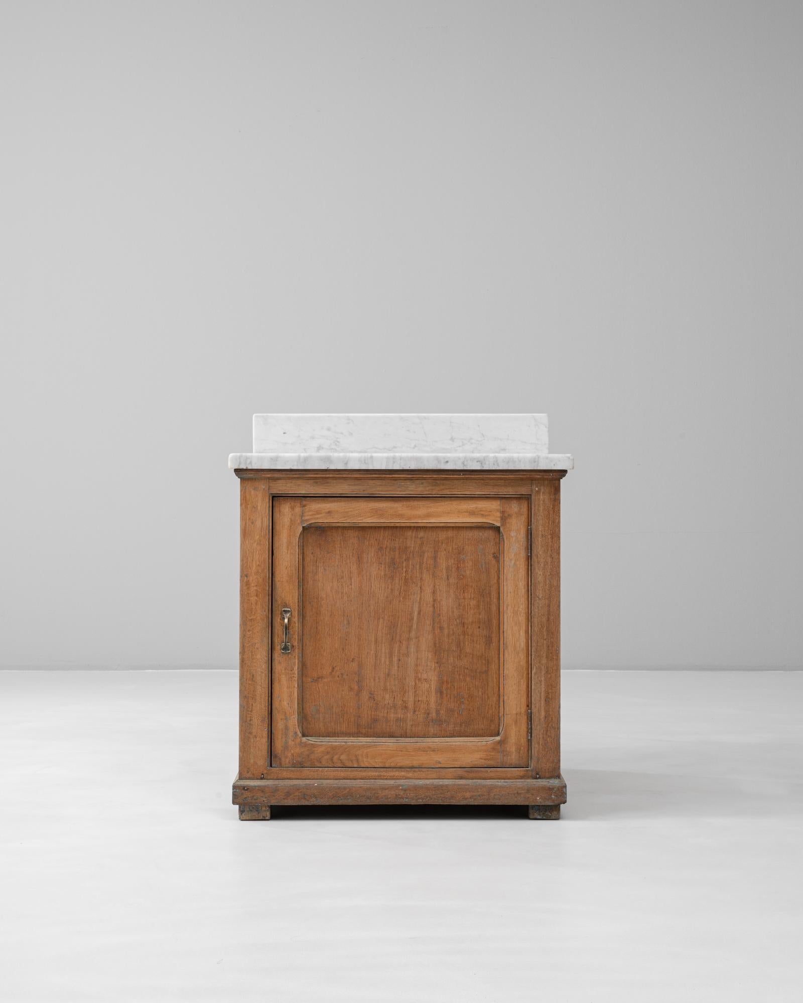 Questo buffet francese degli anni '20 in legno con piano in marmo è un esempio di eleganza sobria e design pratico. Realizzato in legno massiccio, il pezzo presenta un'anta a pannelli semplici con sottili modanature, che si apre per rivelare