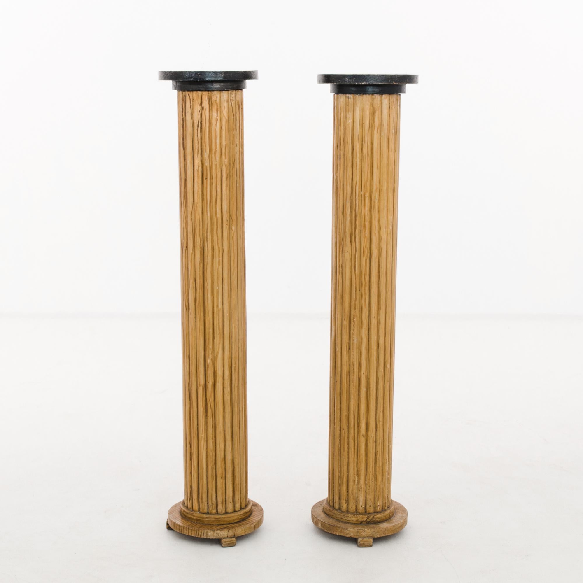 A pair of wooden pedestals from France, produced circa 1920. This pair is a set of freestanding doric columns, set upon three toe bases, wearing permanent black caps. At four feet in height, once this duo is installed, they form a kind of gate,
