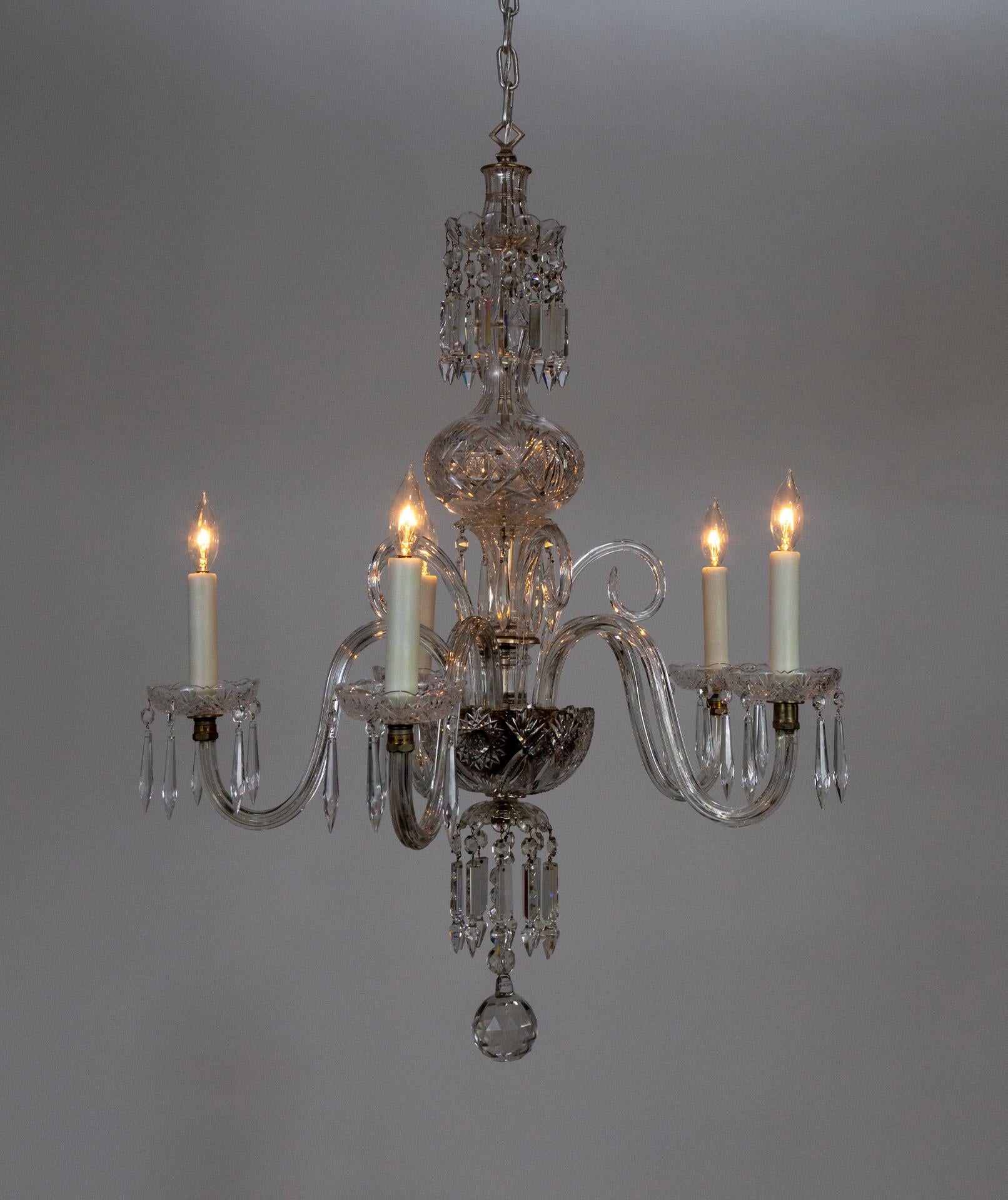 A Georgian style chandelier with waterfall oriented crystals on the top and bottom, intricately cut crystal bowls and bobeches, crystal scroll arms and curling accents, and a large, faceted ball finial. Made in Italy in the early 20th century; in