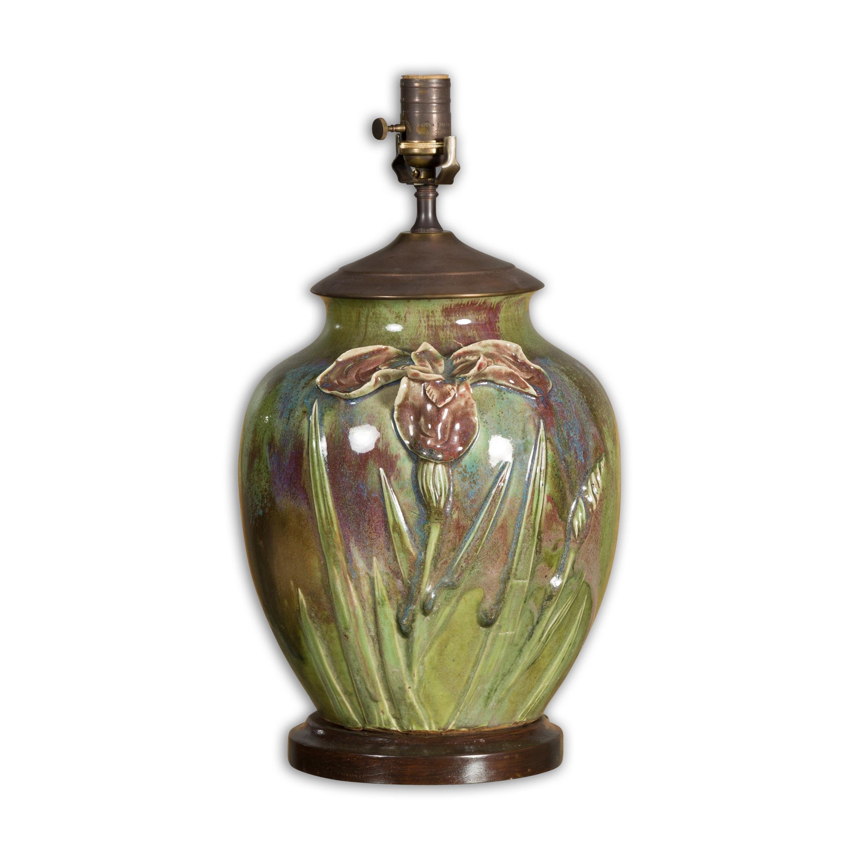 A green glazed 1920s pottery table lamp with raised floral motif, brown accents and circular wooden base. Evoke a sense of classic elegance with this exquisitely designed 1920s green glazed pottery table lamp. This meticulously crafted luminary