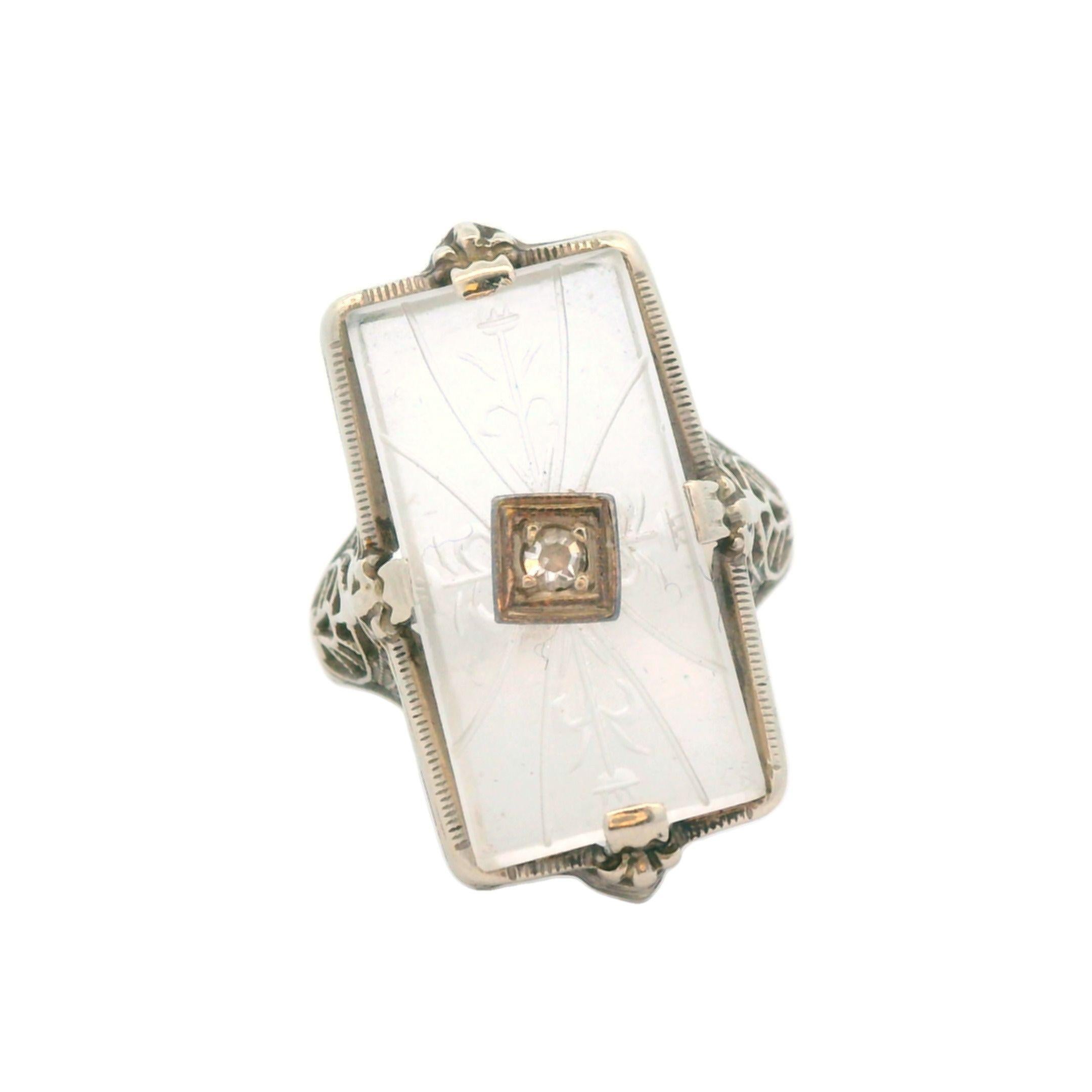 This is a beautifully hand carved crystal and diamond filigree ring, made in the 1920s, in 14k white gold. This gorgeous ring is set with quartz rock crystal that has been turned into a work of art through lovely hand engravings. The center stone of