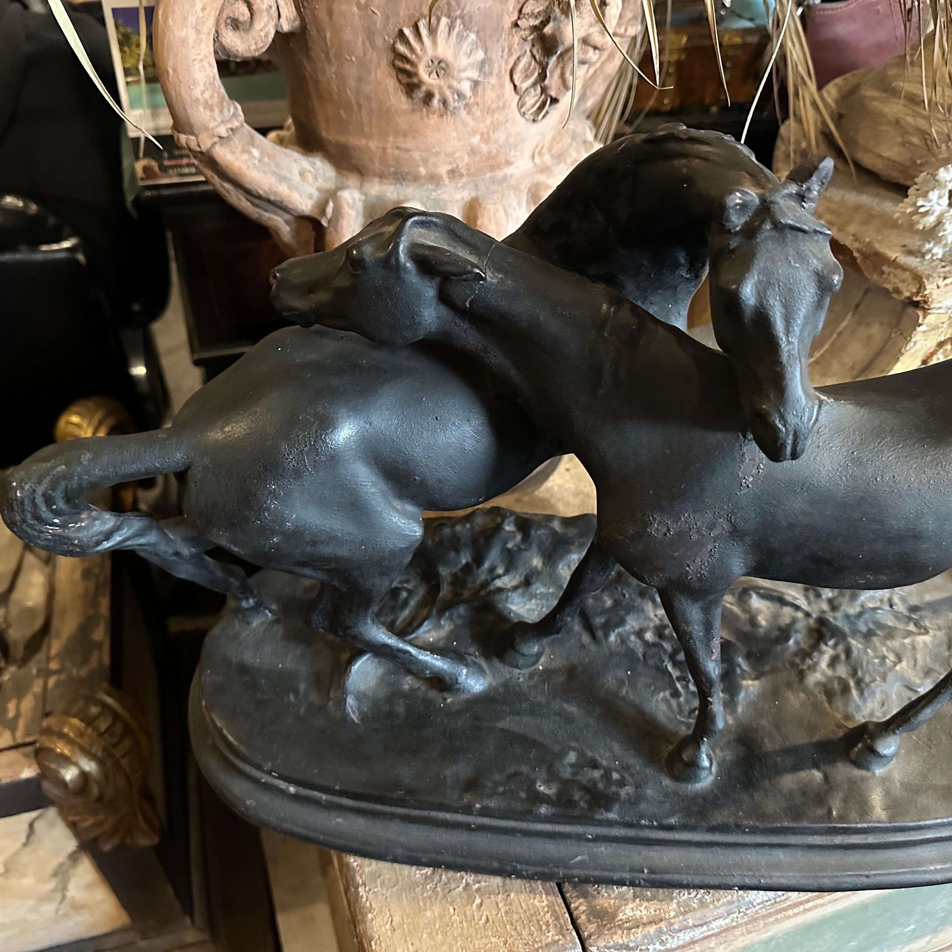 Se trata de una escultura artesanal de terracota con dos caballos, pintada de negro, creada en la década de 1920 en Italia. La obra de arte muestra a los caballos entrelazados en una pose dinámica, de pie sobre una base ovalada que imita el terreno