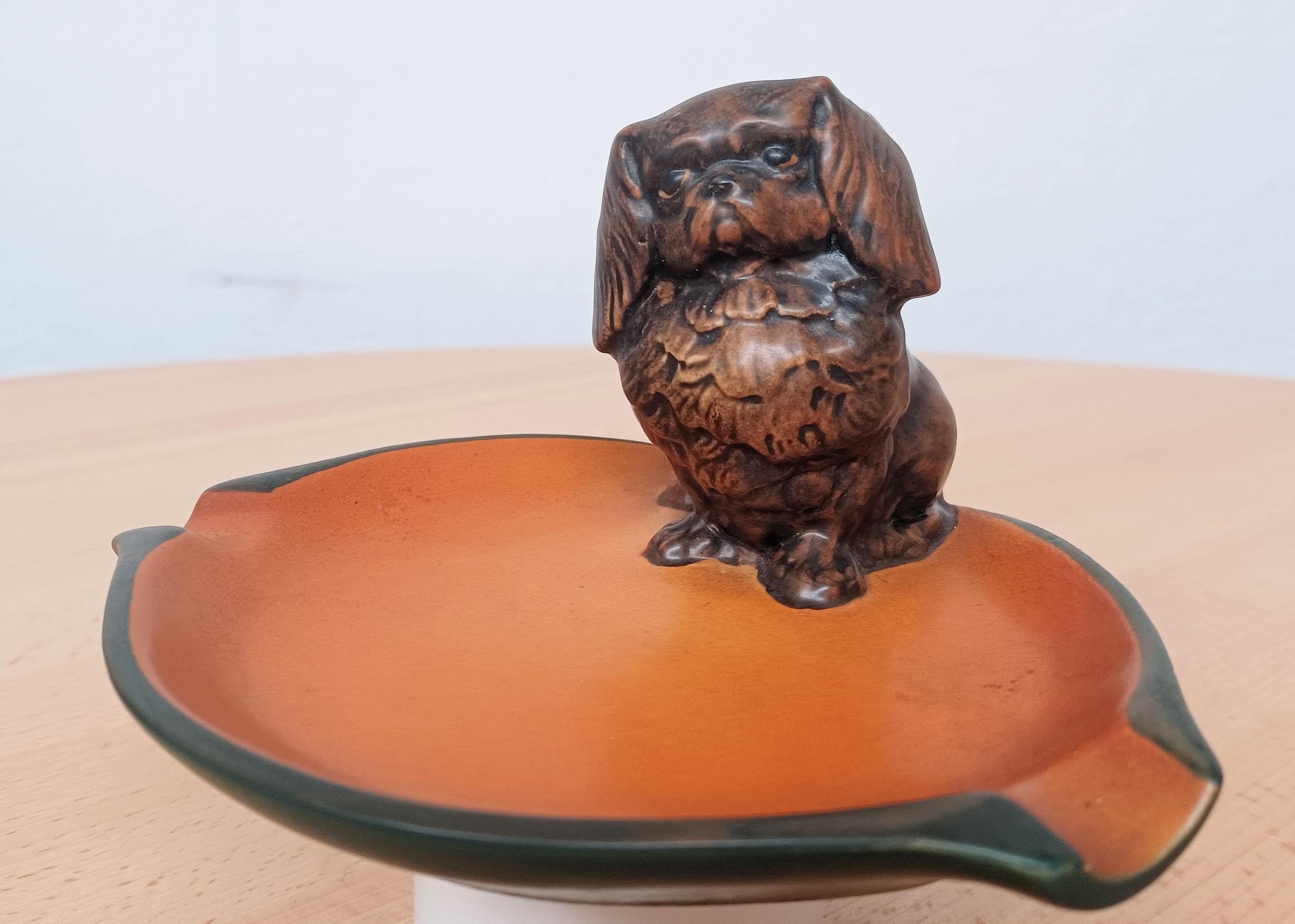 Chien pékinois Art Nouveau danois des années 1920 fabriqué à la main  Cendrier / bol de P. Ipsen Enke. 

Le cendrier / bol art nuveau représente un chien pékinois bien vivant et a été conçu par un artiste appelé West en 1927.

Ipsen (1843 - 1955)