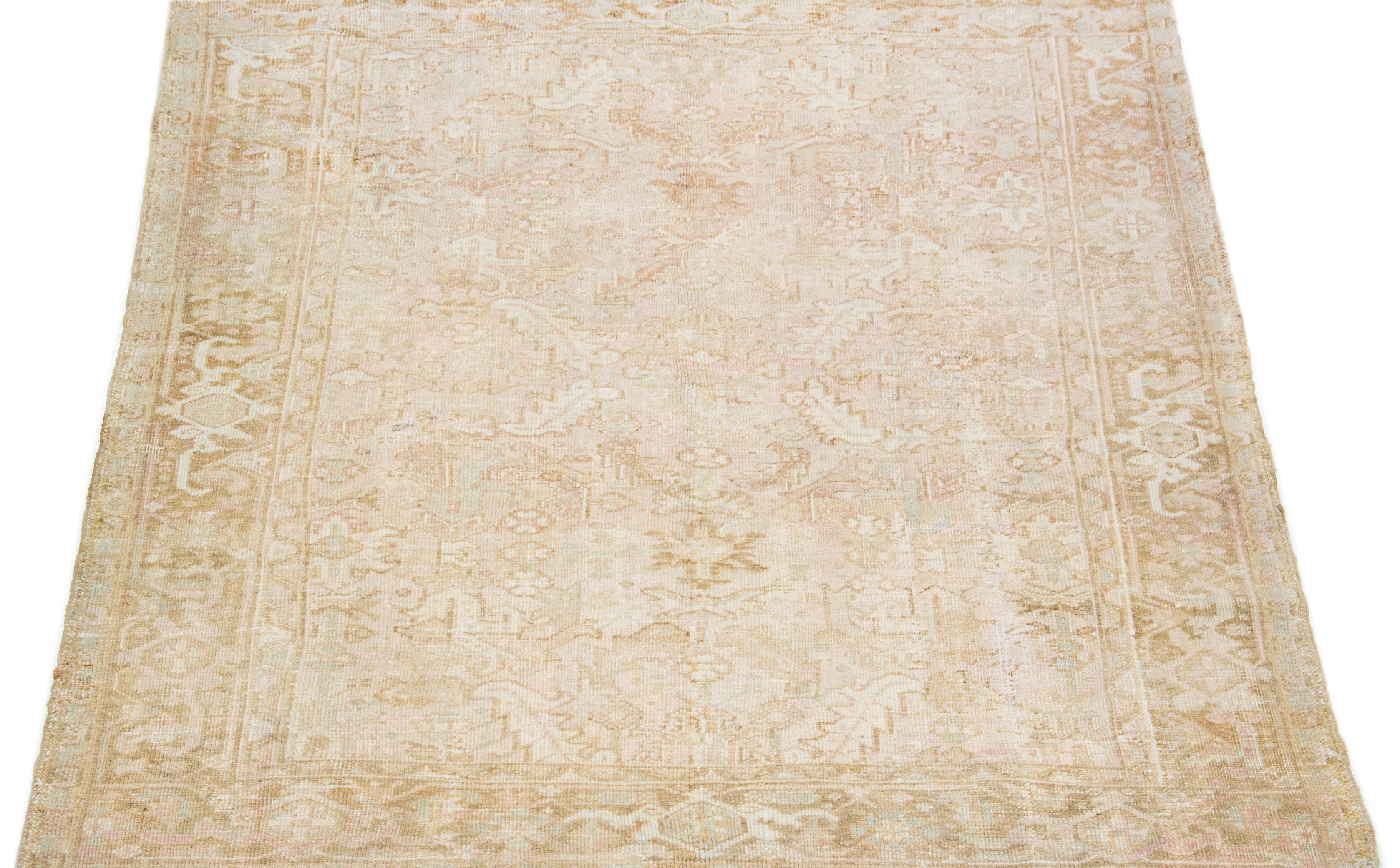 This Persian rug boasts a splendid all-over design with an eye-catching geometric floral pattern in shades of blue and brown set against a soft peach and beige field. Using premium hand-knotted wool, this antique Heriz rug radiates eternal class and