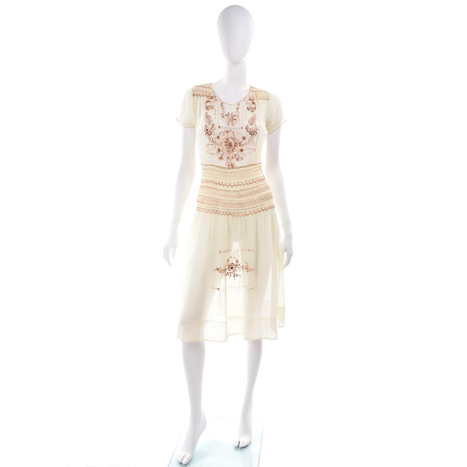 This is a pretty vintage 1920's Hungarian peasant dress. This dress is made of embroidered cream cotton voile and has rows of decorative smock pleating at the waist and on the short sleeves.. This lightweight vintage dress has brown, peach, and tan
