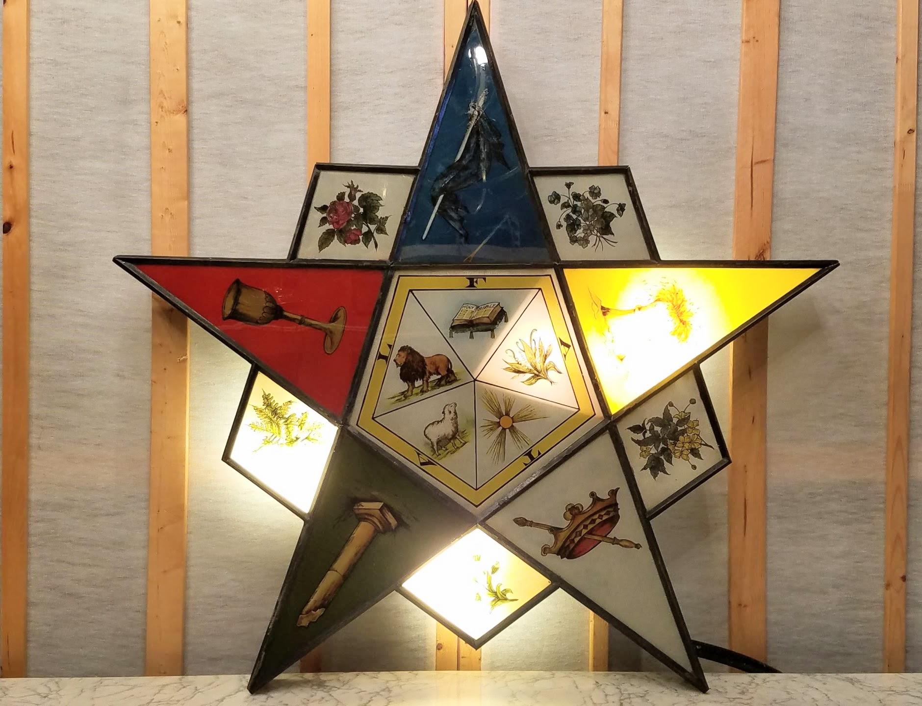 Enseigne lumineuse en fer-blanc avec une peinture inversée sur étoile en verre pour l'Eastern Star du Temple maçonnique des années 1920.
L'enseigne est présentée montée sur son trépied d'origine en tube métallique qui roule sur des roues en bois et
