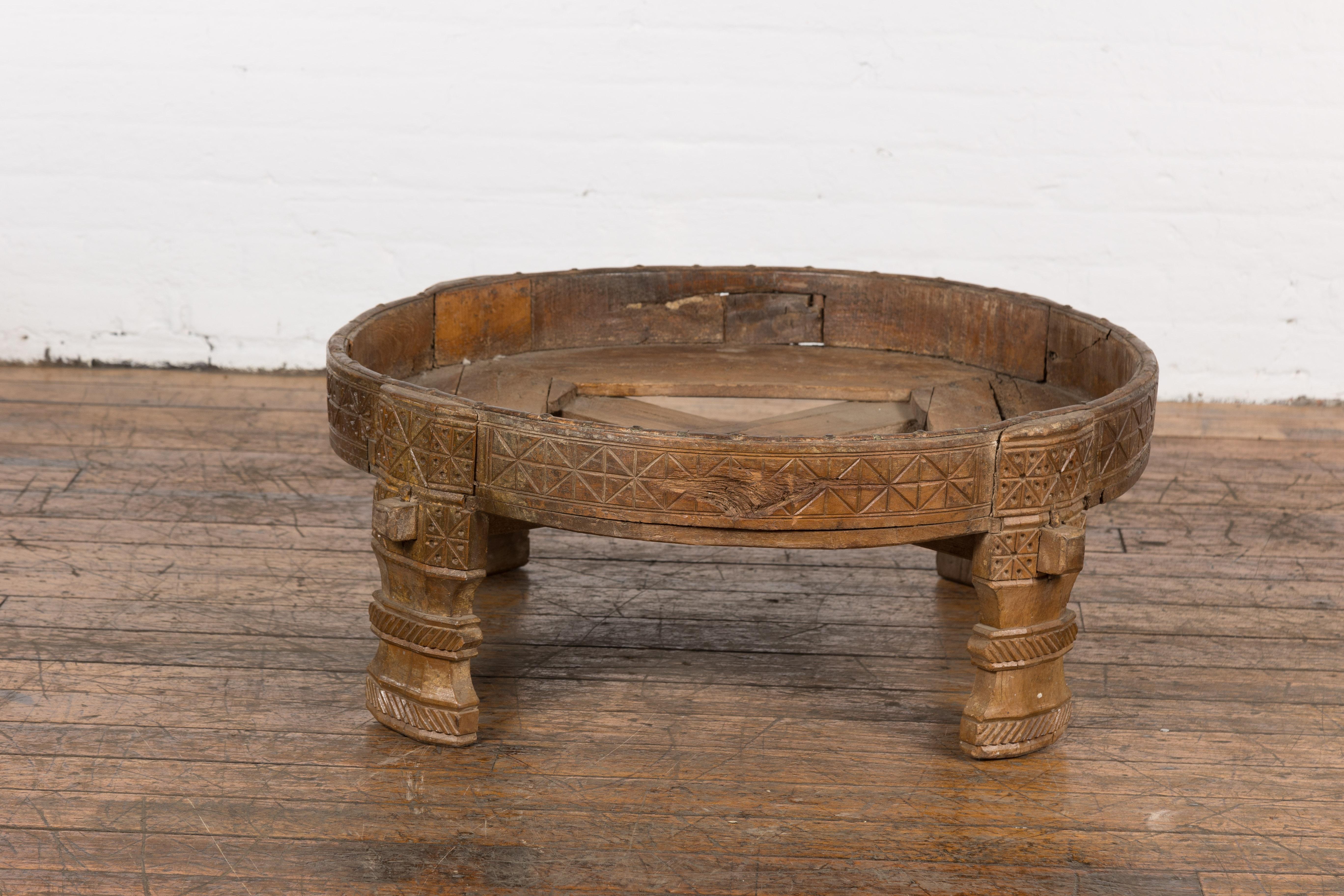 A Tribal Indian rustic Chakki grinder table from the 1920s with hand-carved geometric motifs, open center, carved feet and weathered patina. This tribal Indian rustic Chakki grinder table from the early 20th century is an exceptional blend of