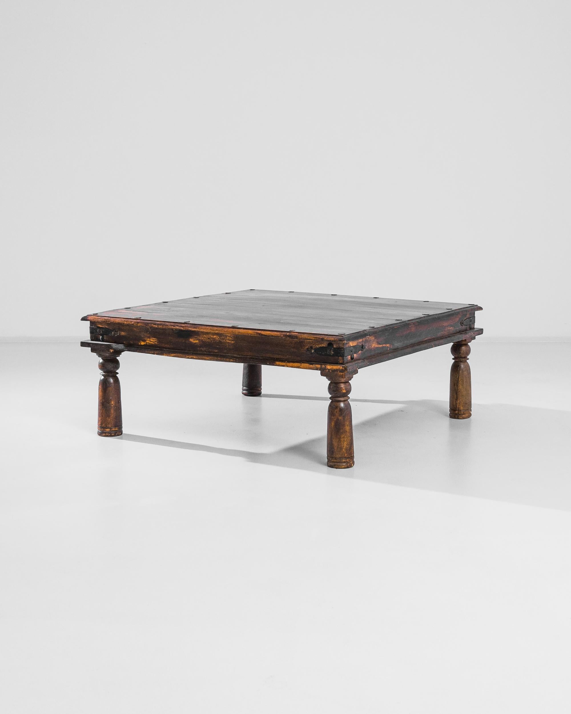 A wooden coffee table from India, produced circa 1920. A finely turned antique from the British Raj: low-slung coffee table with iron brackets clamping the corners standing on four cup and ball legs, featuring a border of twenty iron rivets around