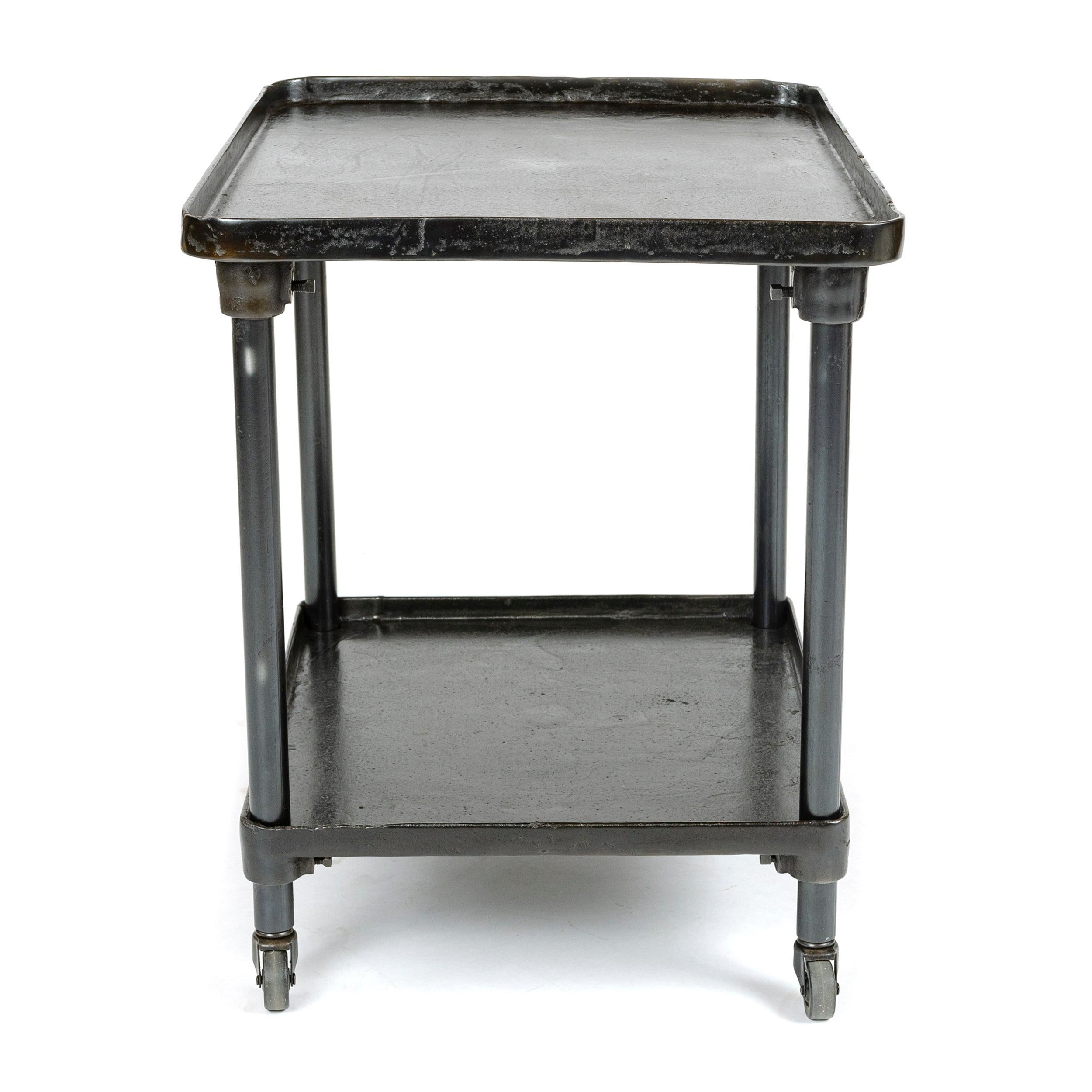 Two-tier industrial cart with an oil and wax blackened finish on castors with height adjustable lower shelf. Each shelf has rounded corners with a one inch lip around its perimeter. Diversifying from steam engine production, the J.T. Case Engine Co.