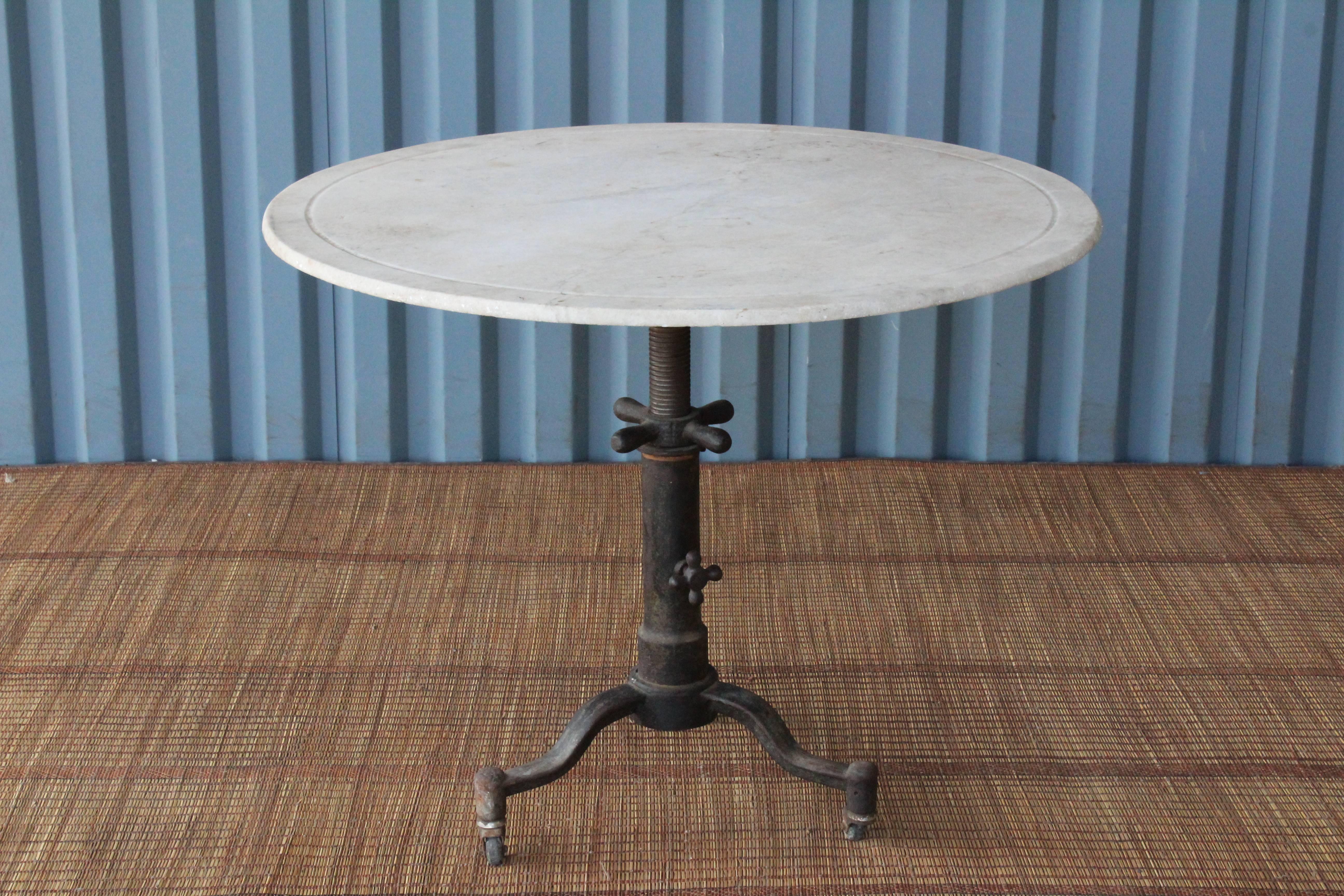 1920s Industrial cast iron table base on rolling casters with an antique marble top. This table is height adjustable and can be used anywhere between 25.5 inches high to 30 inches high. Marble top has age appropriate patina. Table base has slight