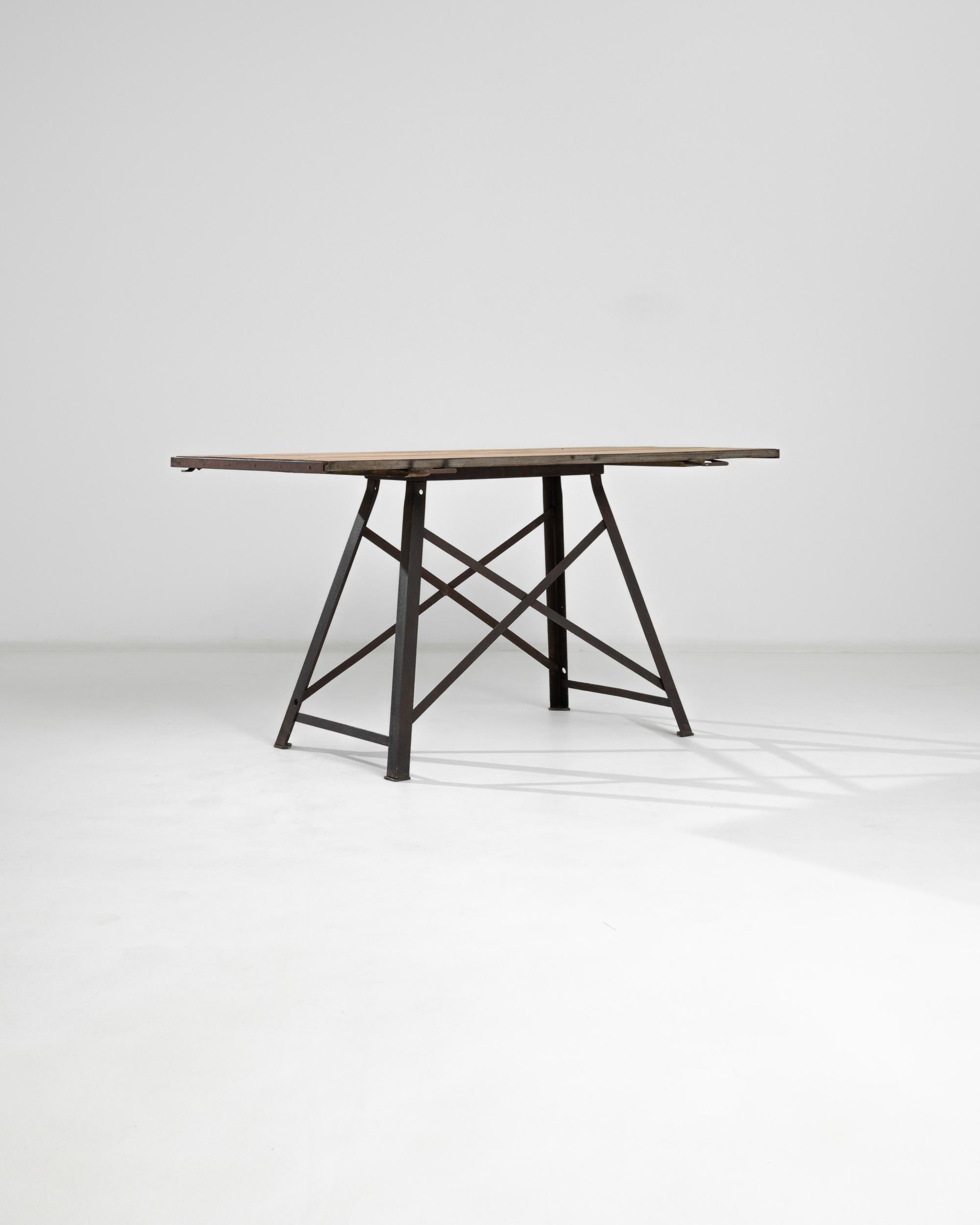 A table from 1920s France with a stylish, angular silhouette. The metal cross-bars of the trapezoid frame evoke the lattice of the Eiffel tower, lending a cosmopolitan inflection. Curved metal handles and riveted girders accent the tabletop,