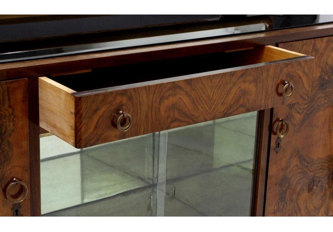 Grand Italian Art Deco sideboard or buffet, circa 1925. A rectangular framed mirror over a black glass top, two doors flanking a central drawer over a sliding glass display area, all raised on shaped deco side supports with a central inward curved