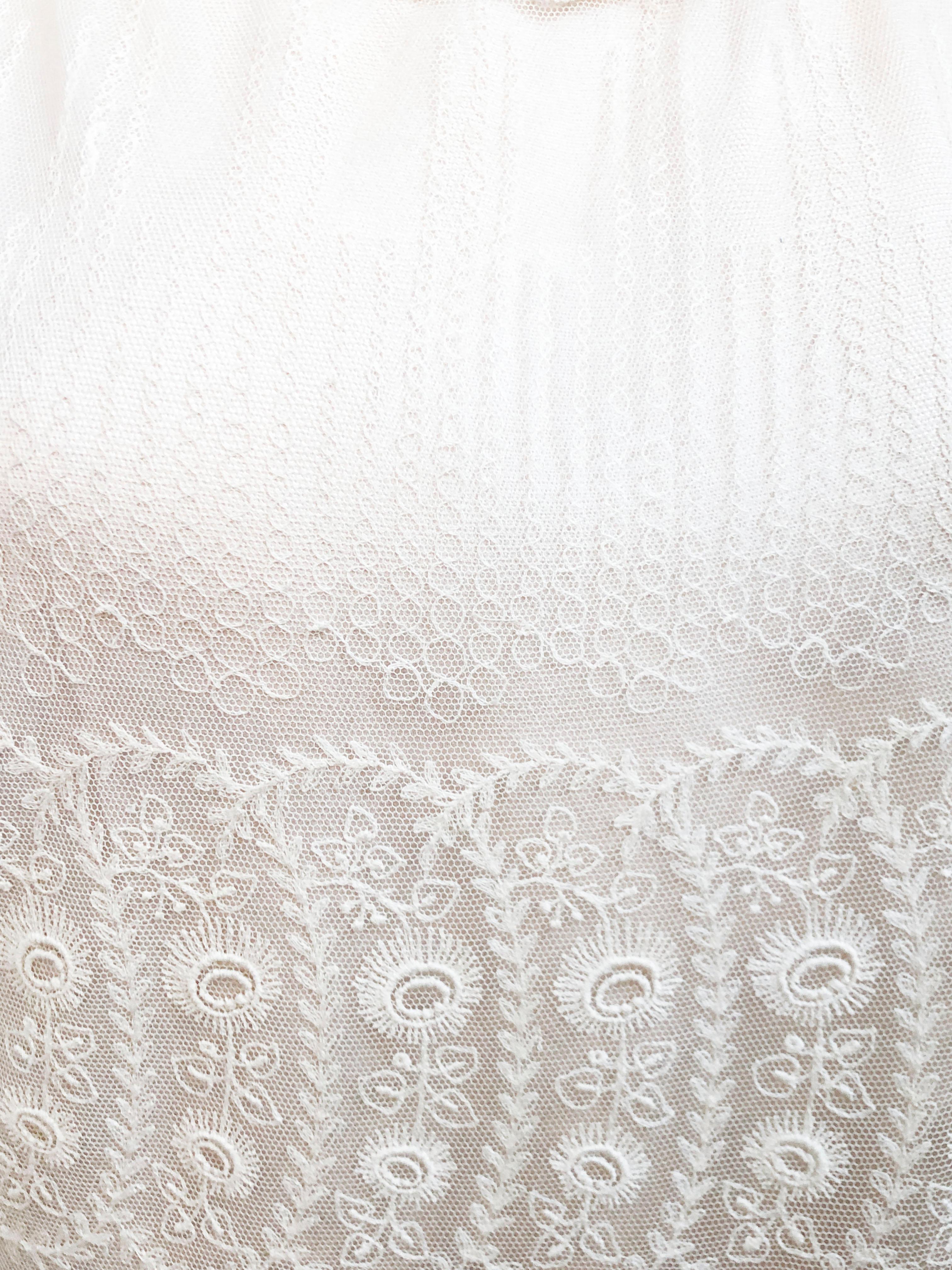 Abito in pizzo con intricati motivi floreali e di righe, foderato con un morbido jersey di seta rosa. La silhouette a vita bassa accentua la gonna a strati di pizzo e le rifiniture in pizzo intorno al collo e alle maniche.