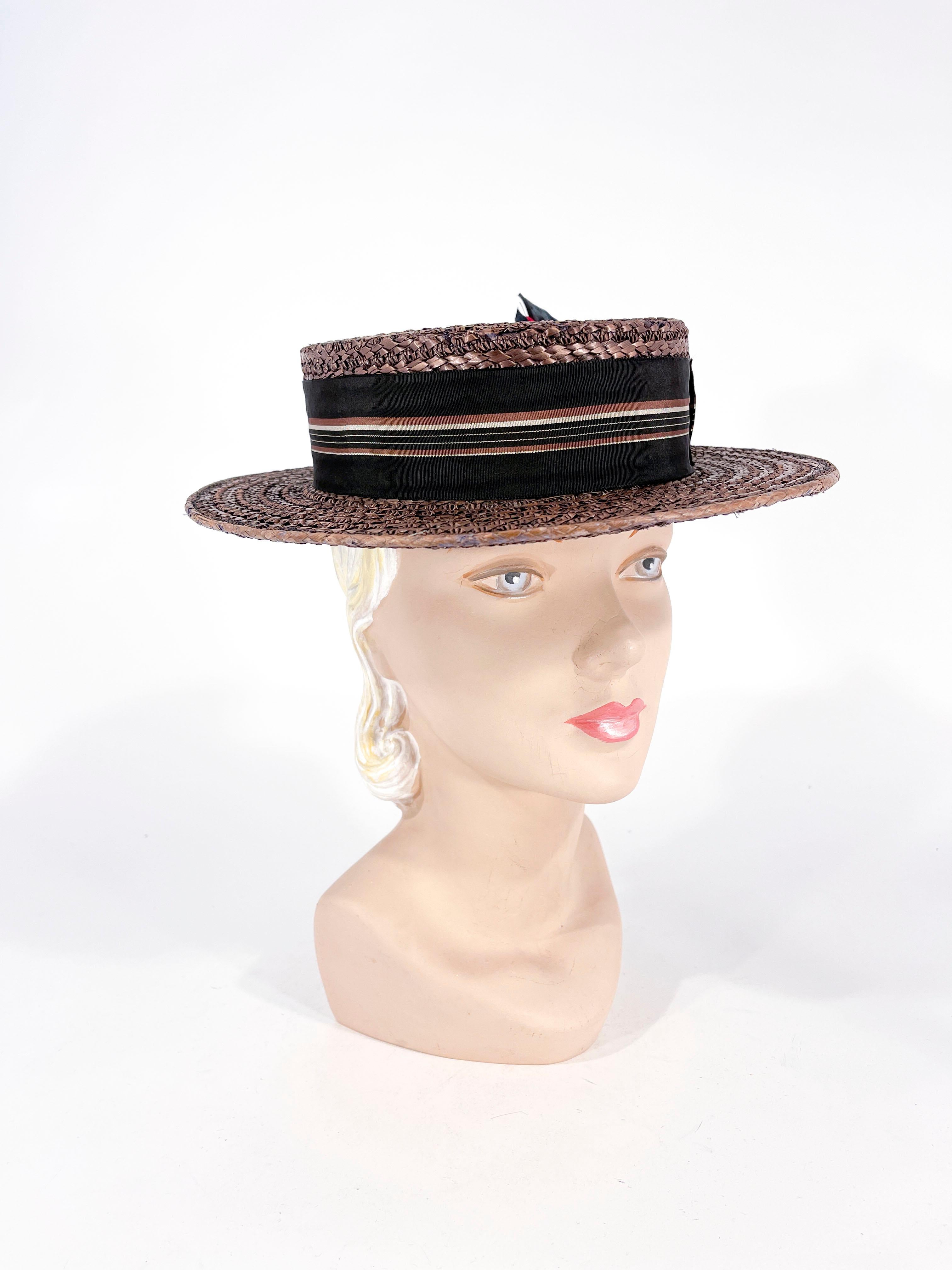 1920s Art Deco Ladies boater hat of handwoven straw that has been tinted a cocoa brown color. The shallow crown of the hat is decorated with a multi-striped and colored grosgrain hat band and an enlarged handmade bow finished with a feather accent.