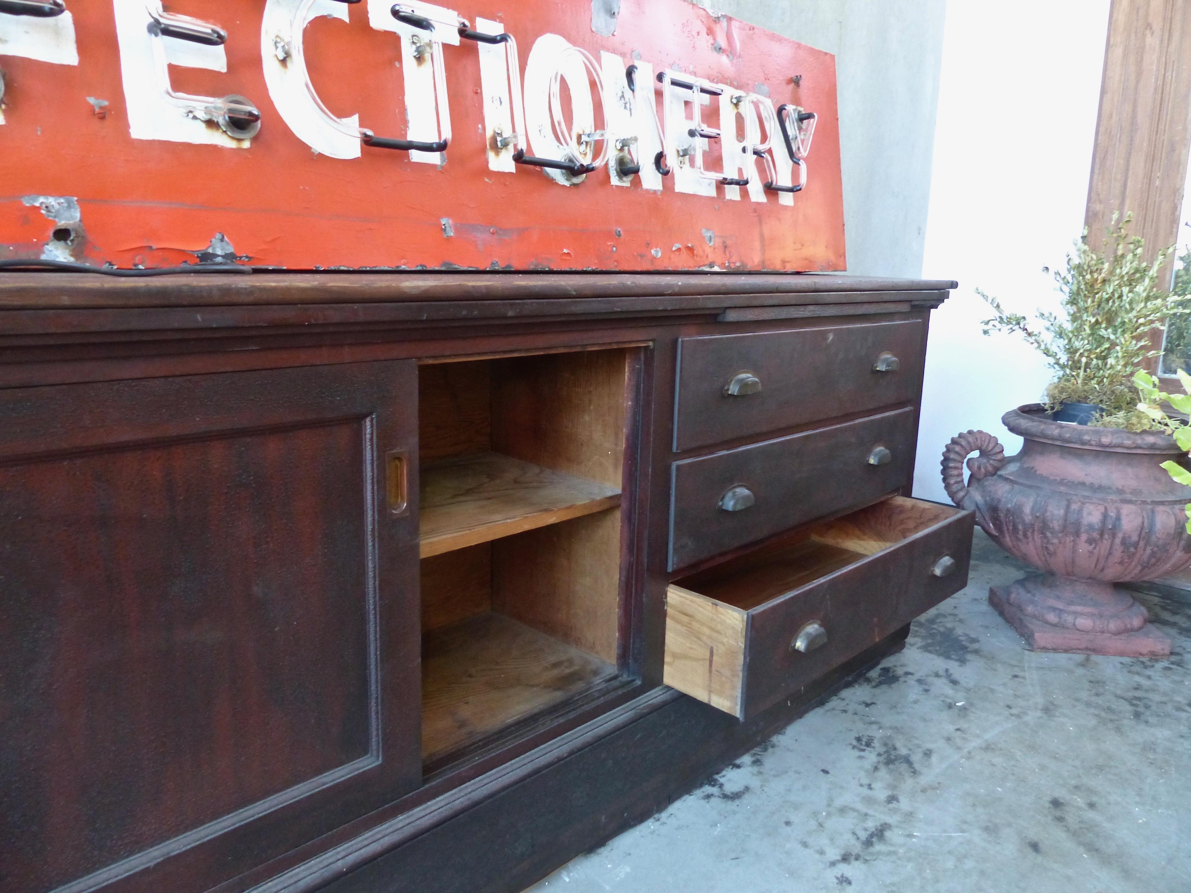 An oversized store counter, circa 1920, with six drawers as well as shelves and two pull-out ‘desk tops’. Made from fir, with an untouched, age-cracked surface and original brass hardware. Dimensions: 32 H” x 124 W” x 19 D”.
