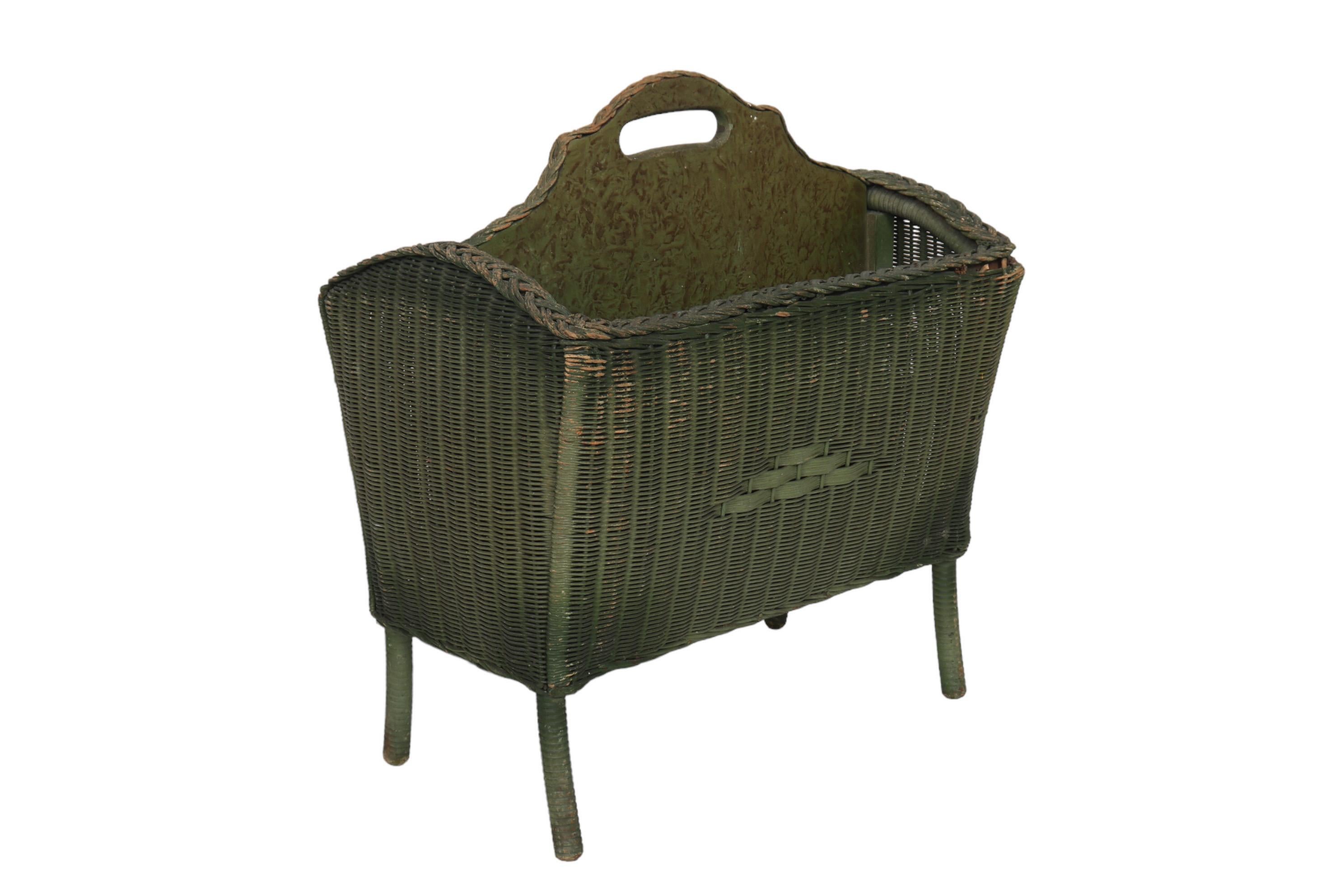 A 1920’s wicker newspaper and magazine rack made by Lloyd Loom of Menominee, Michigan. Decorated with an open wicker braid around the top edge and over a central wooden divider with a central handle. The divider is painted with a burl-like effect.