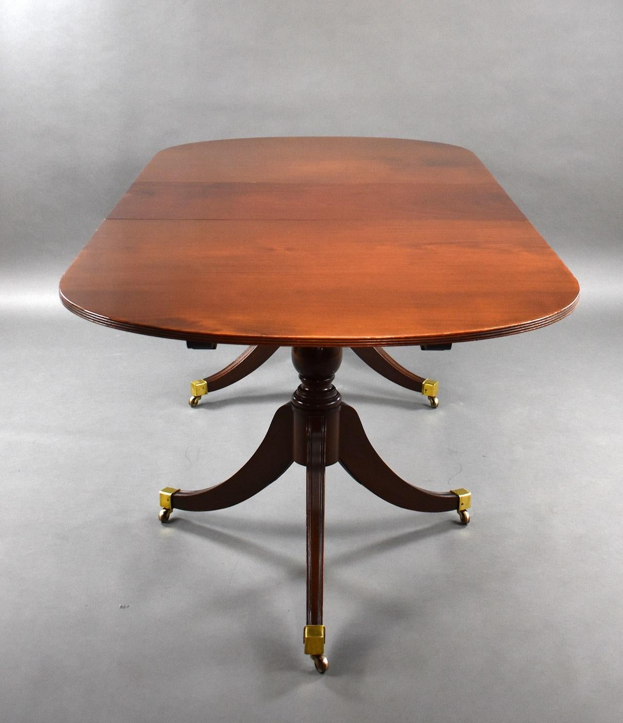 Offered for sale is this 1920s antique mahogany pedestal dining table with one leaf with brass clips standing on splay legs with brass ends on castors.